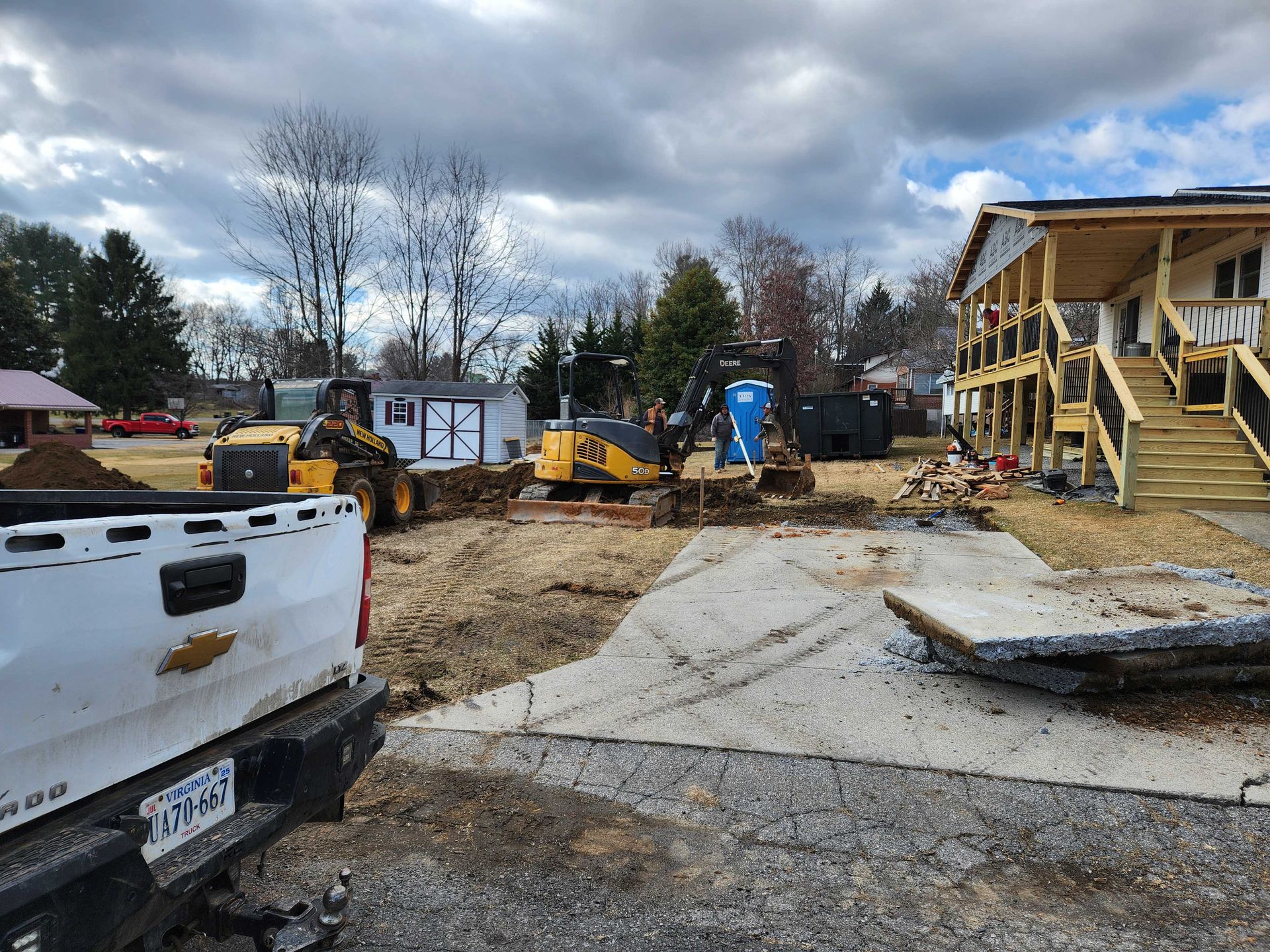 Construction site with heavy machinery, a partially built house, and a pickup truck. Cloudy sky overhead.