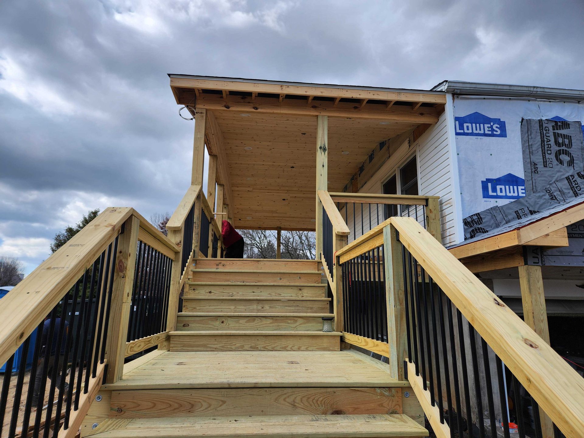 Wooden staircase leading up to a porch with black railings, under a cloudy sky.