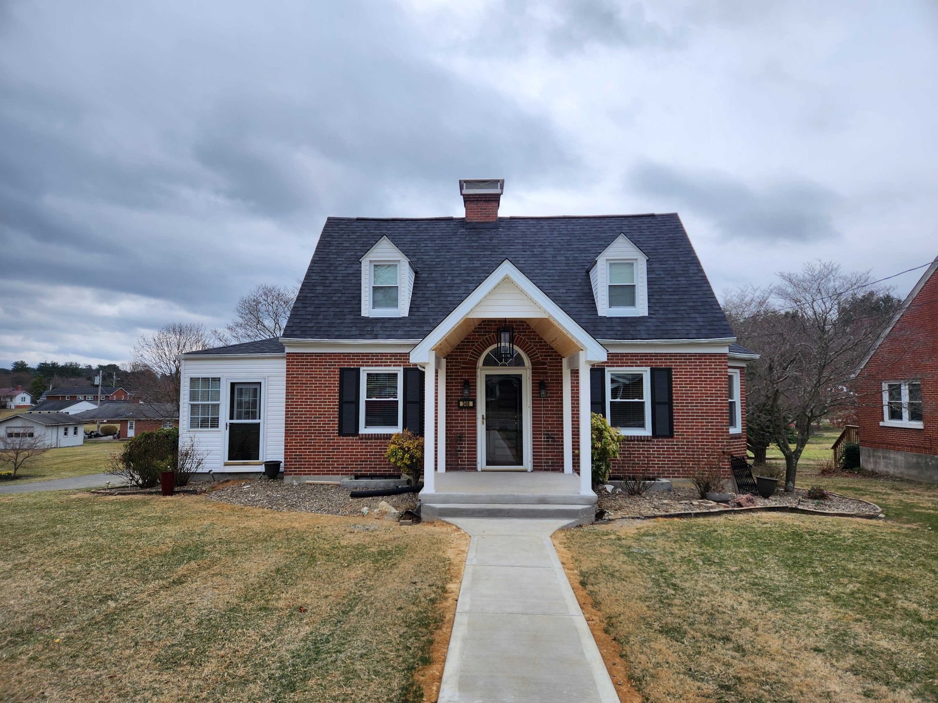 Brick house with a dark roof and two dormers under a cloudy sky.