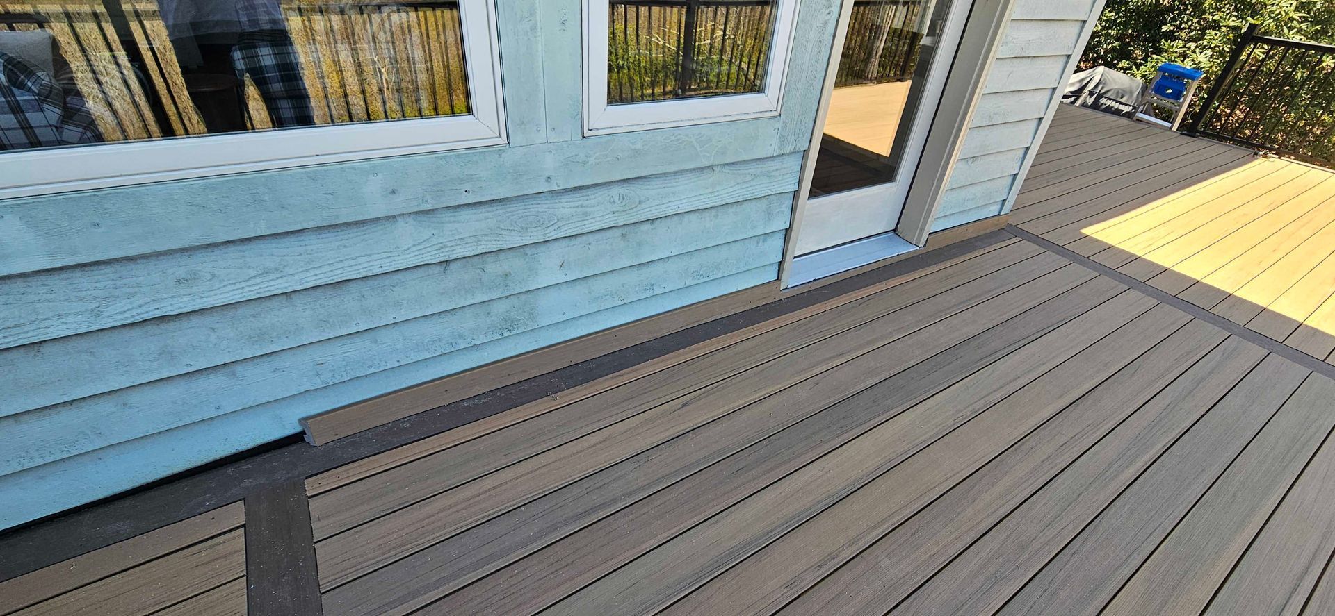 Wooden deck next to a blue house with windows and a glass door.