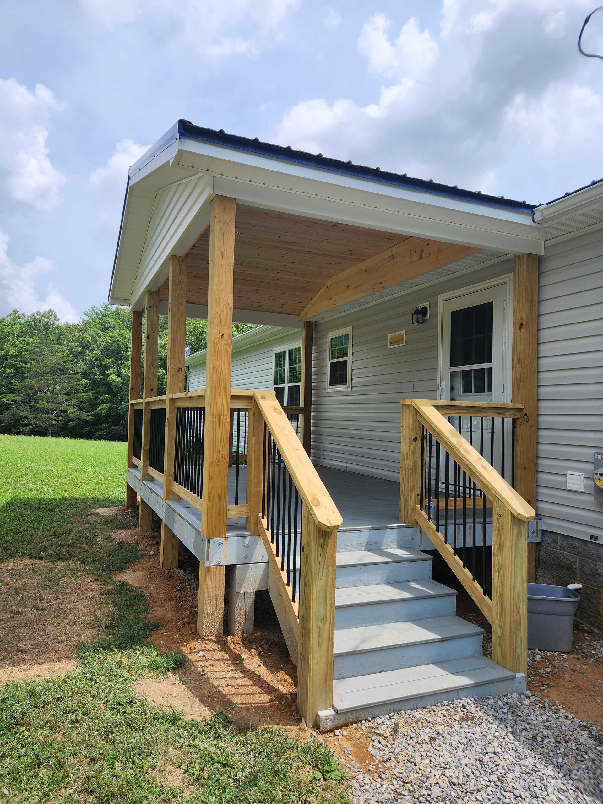 Porch with gray steps, wooden railing and supports, and a covered roof.