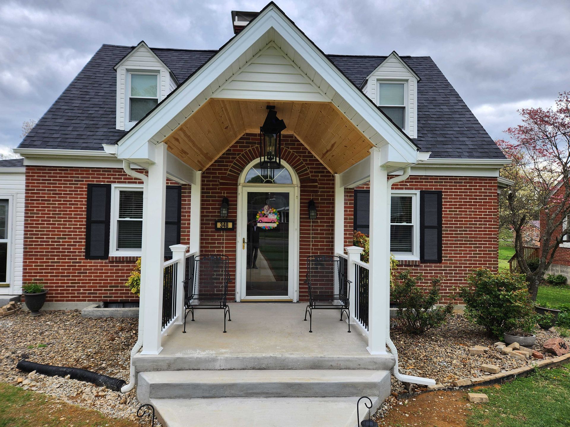 Red brick house with a front porch, black shutters, and a black roof.