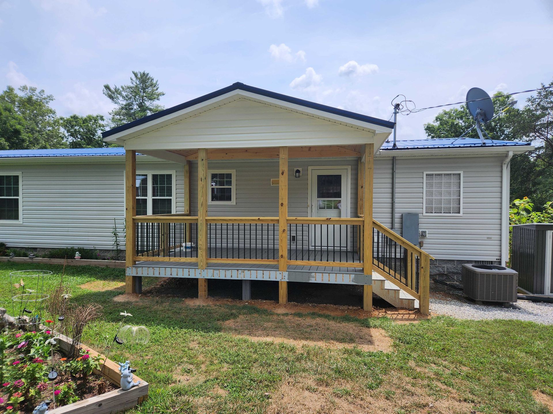Ranch-style house with a front porch. Light gray siding, dark blue roof, wooden deck, and black railing.