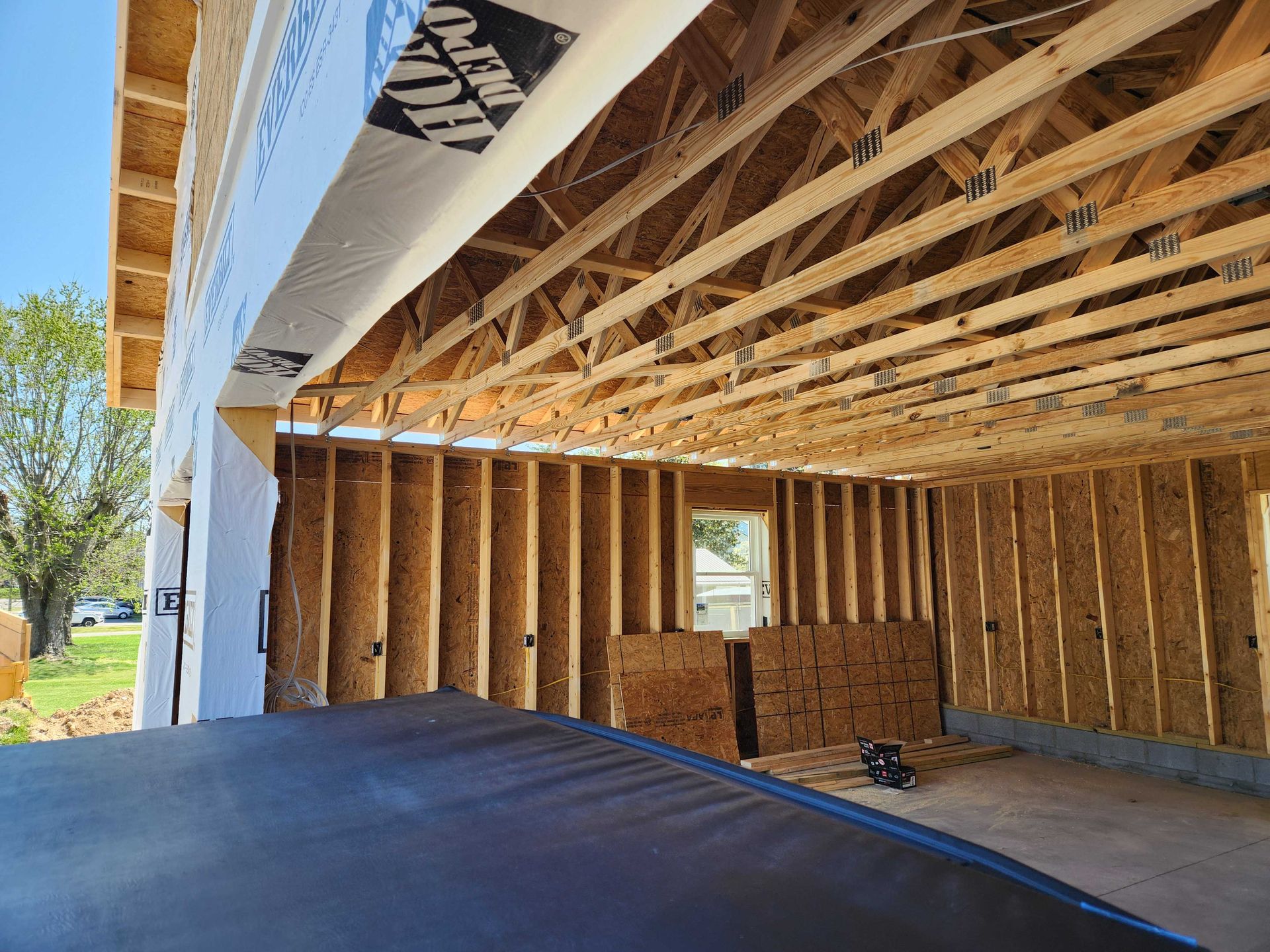 Construction of a garage with exposed wooden beams, studs, and sheathing; blue sky in the background.
