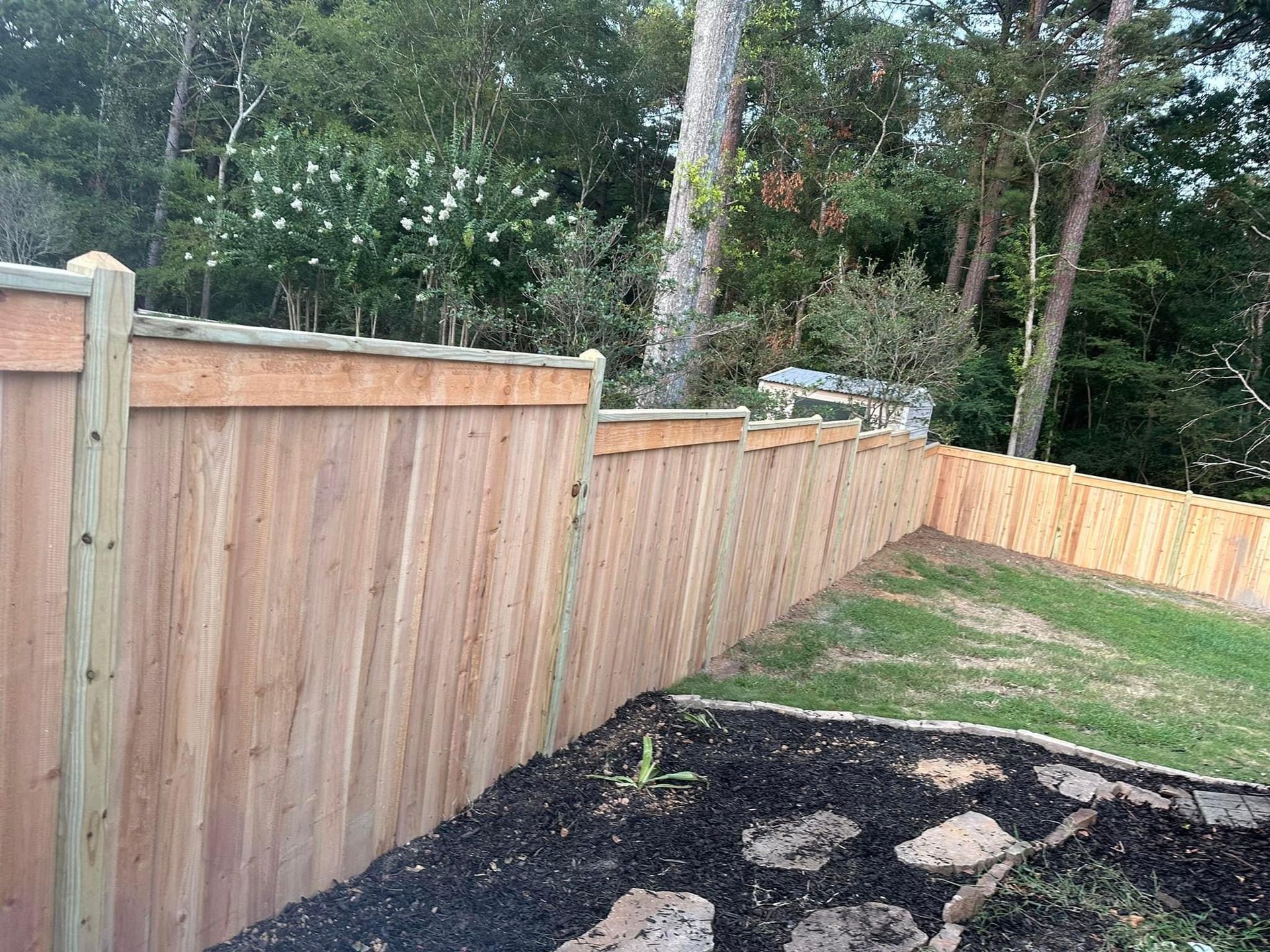 A wooden fence surrounds a backyard with trees in the background.