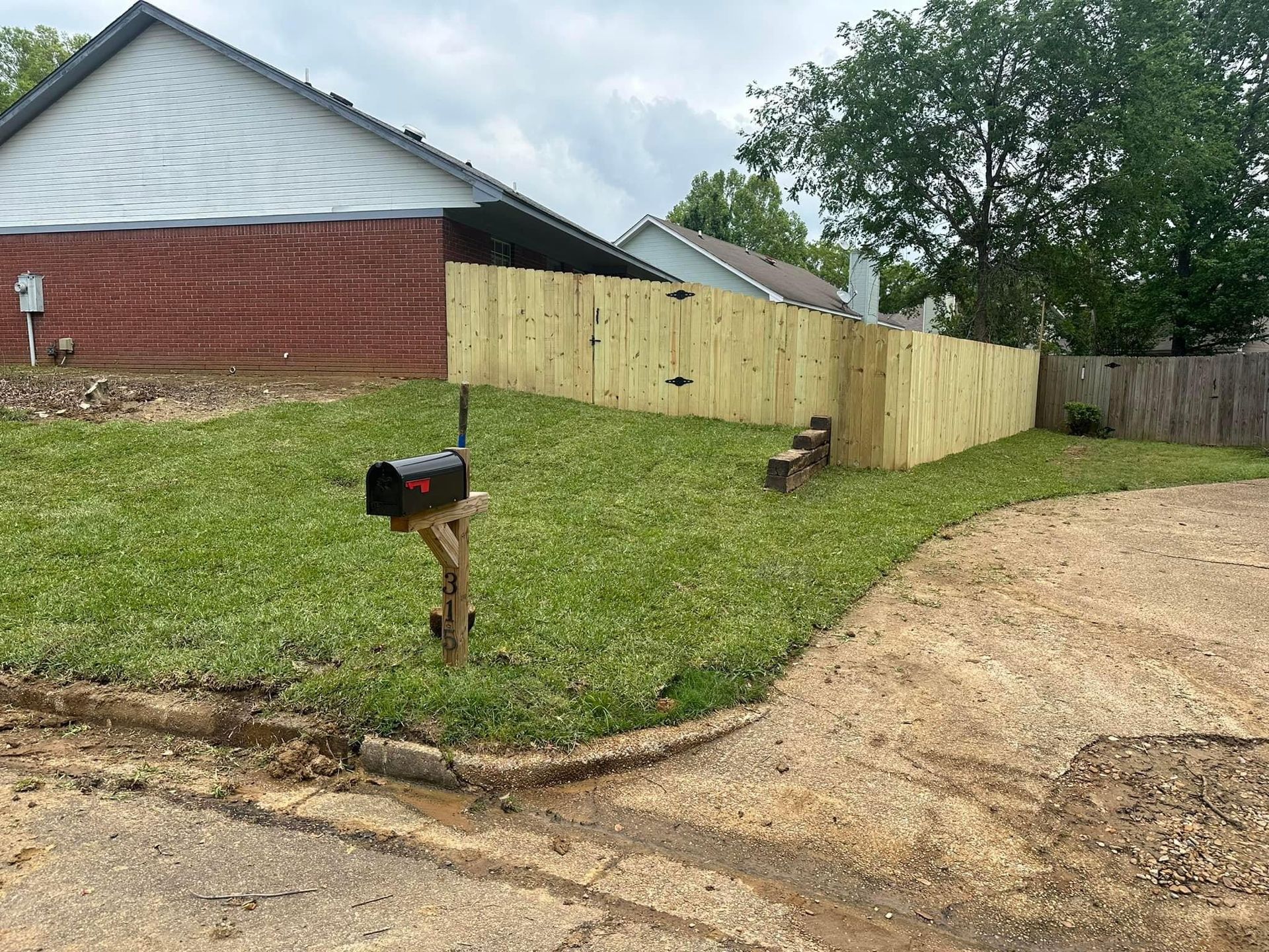A mailbox is in the middle of a lush green yard next to a wooden fence.
