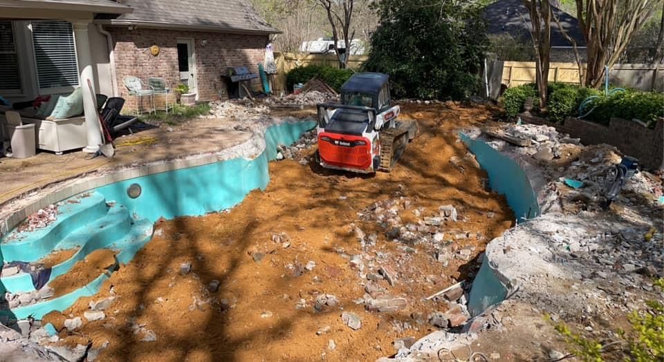 A bulldozer is moving dirt around a swimming pool in a backyard.