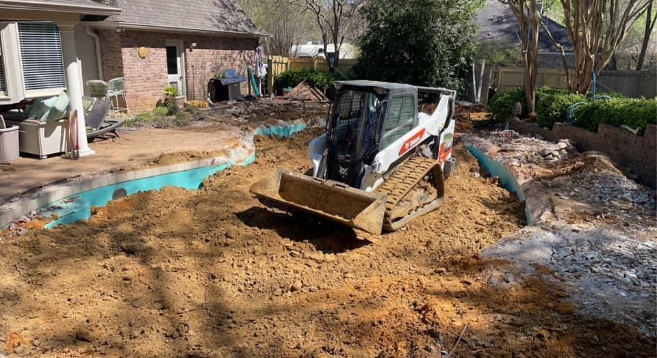 A bulldozer is moving dirt in a backyard in front of a house.