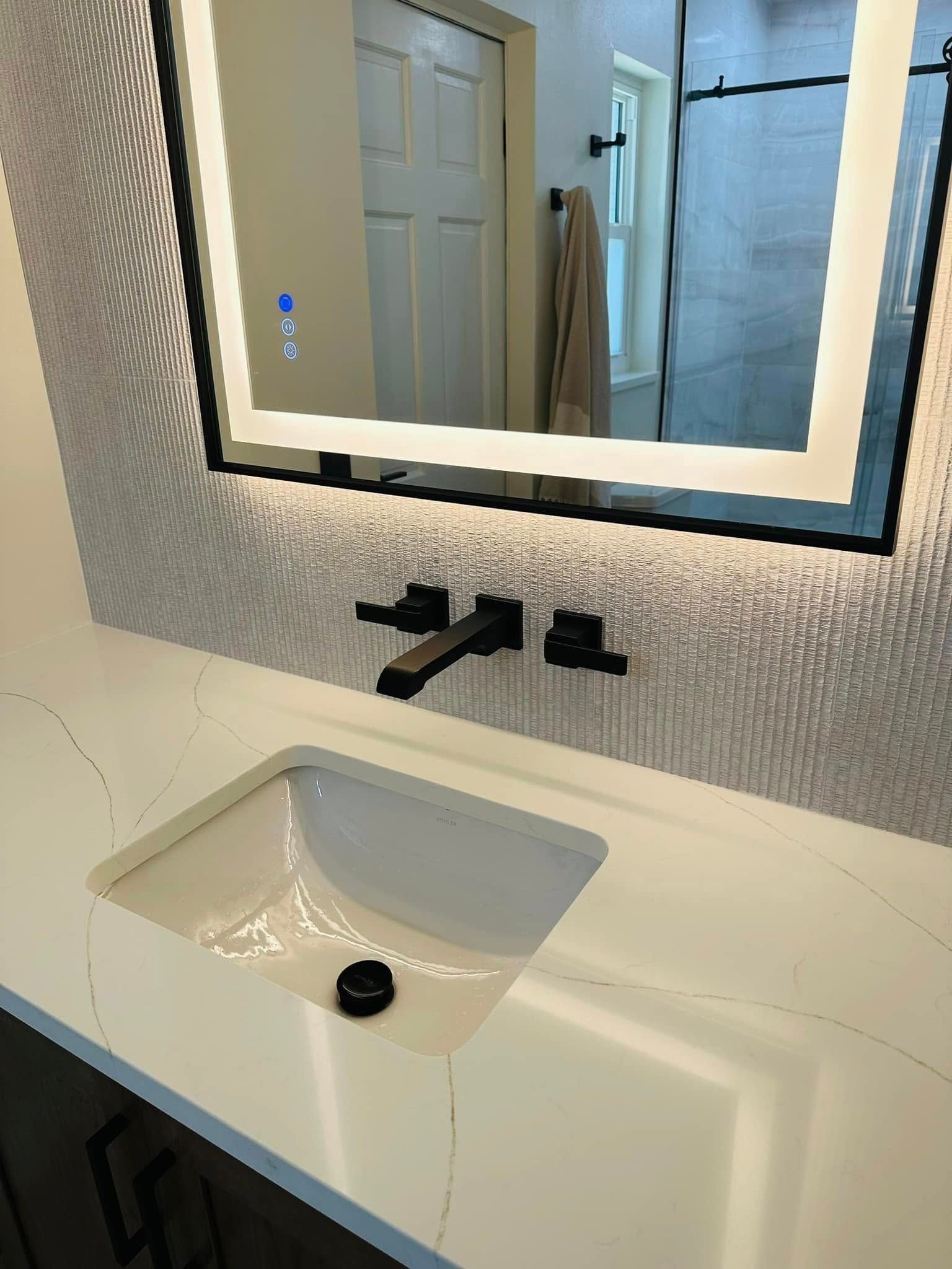 Bathroom vanity with white countertop, integrated sink, black faucet, and backlit mirror.