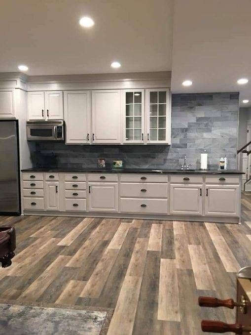 Modern kitchen with white cabinets, gray tile backsplash, stainless appliances, and wood-look flooring.