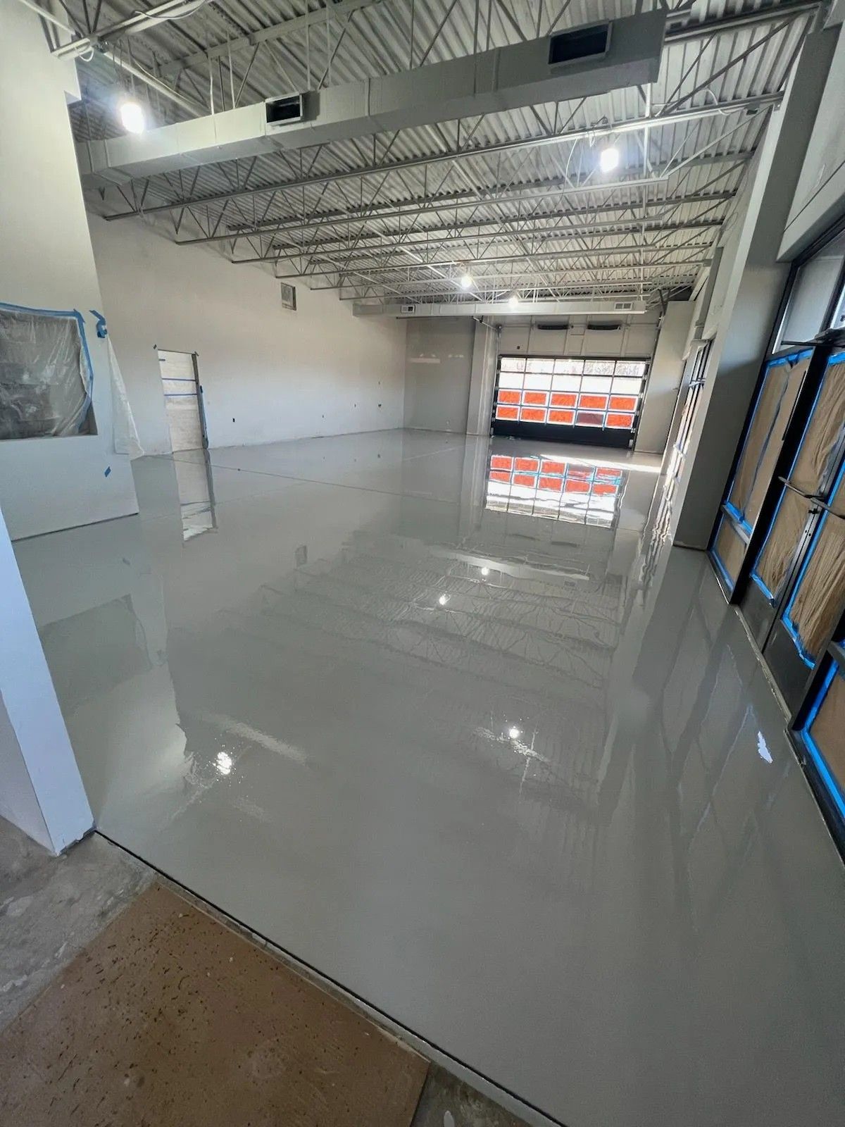Empty commercial interior with glossy white floor, exposed ceiling, and open garage-style entrance.