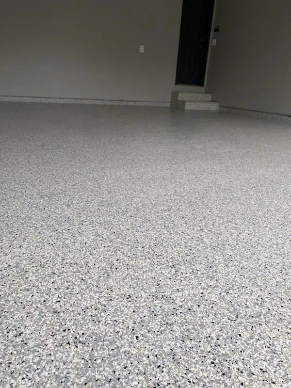 Empty carpeted room with gray speckled flooring, beige walls, and a dark doorway in the back.