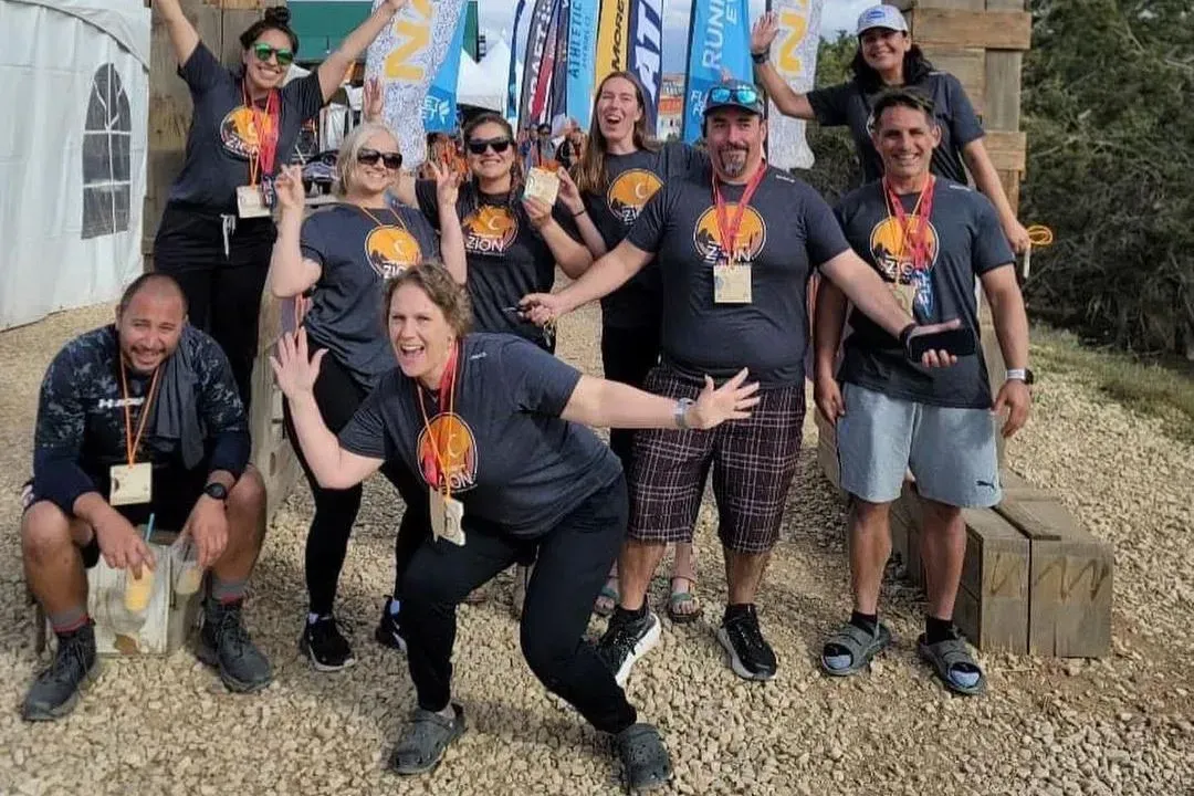 Group of people pose outdoors, wearing matching t-shirts, some making playful gestures.