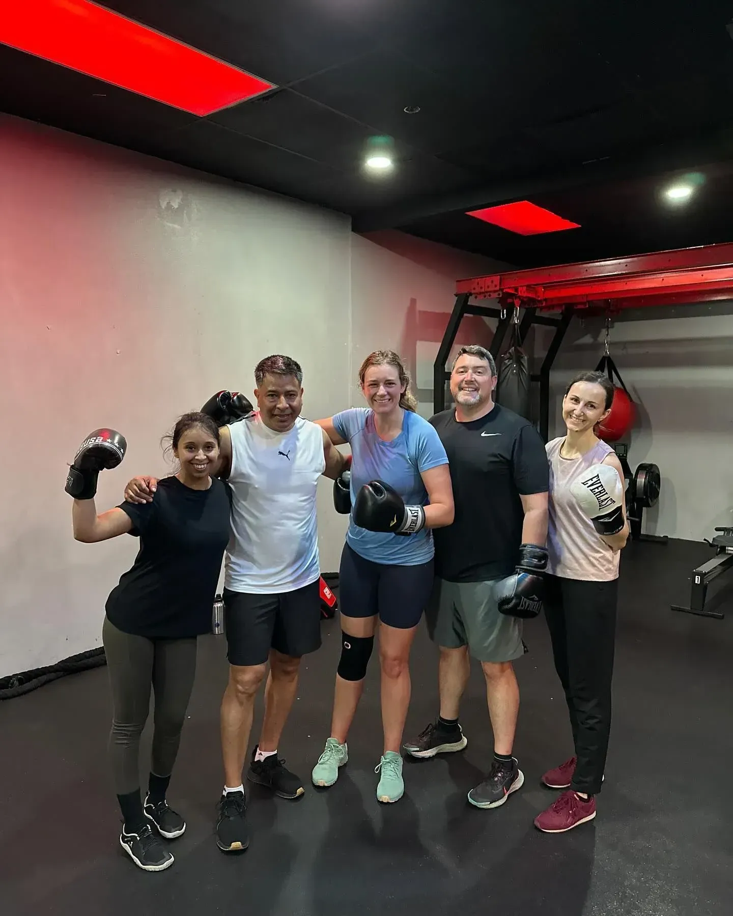 Five people in a gym with boxing gloves posing after a workout.