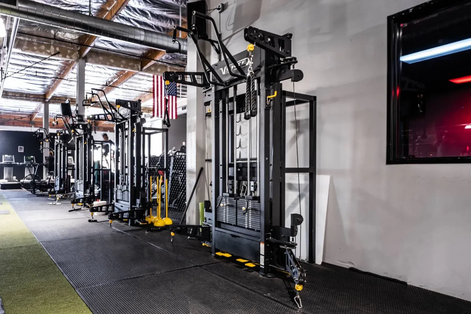 Gym interior with weight machines, an American flag, and a black floor.