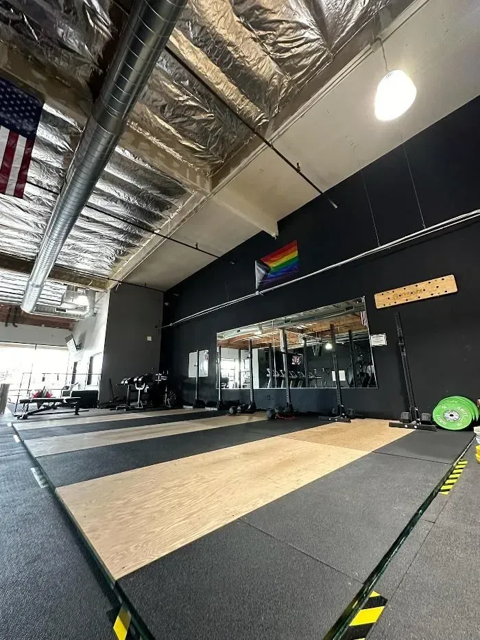 Interior of a gym with weightlifting equipment, an American flag, and a rainbow flag.