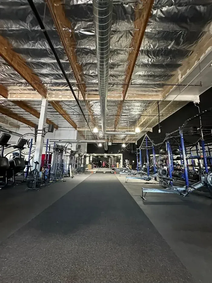 Gym interior with fitness equipment. Metal ductwork and wood beams overhead.