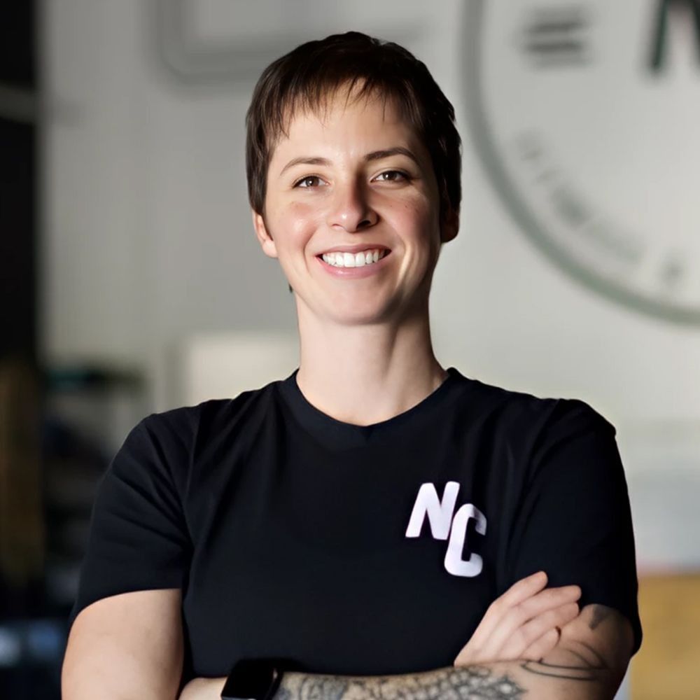 Woman with short hair, smiling with arms crossed, wearing a black t-shirt with 