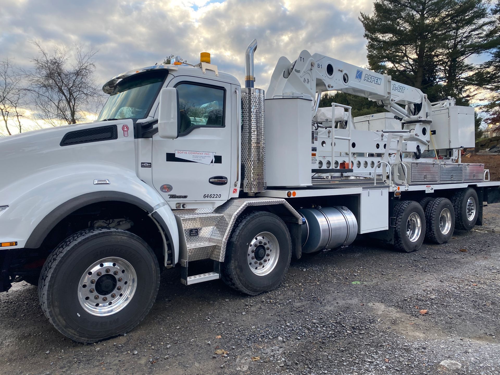 A large white truck with a crane on the back is parked in a gravel lot