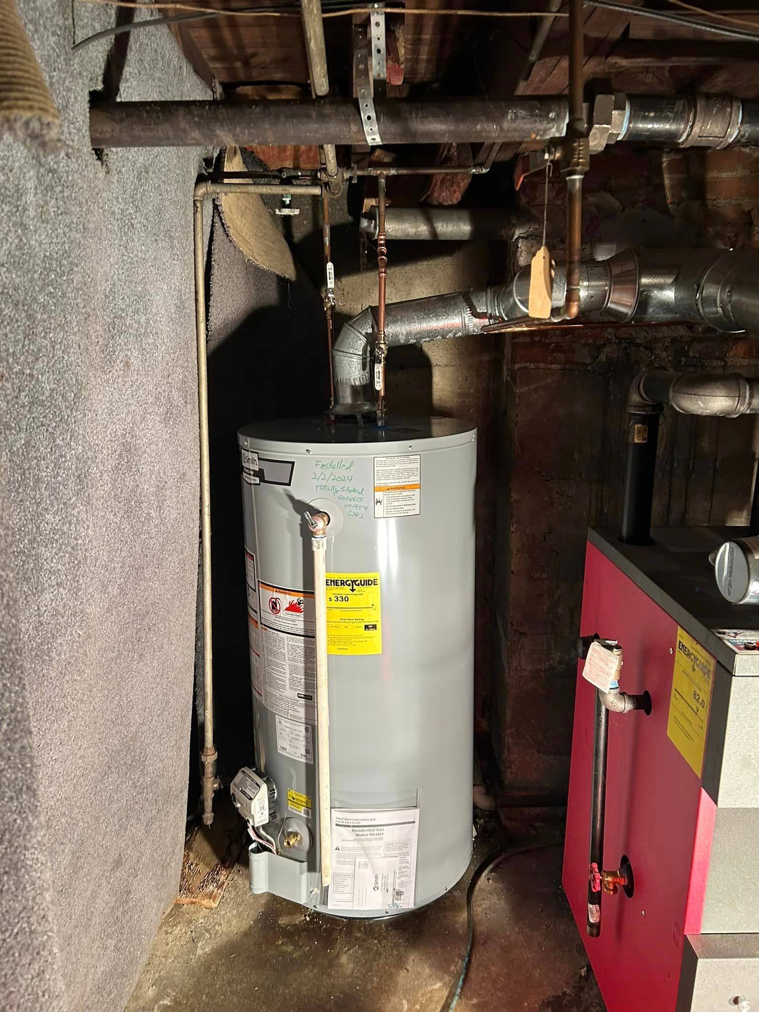 a water heater is sitting in a basement next to a red boiler .