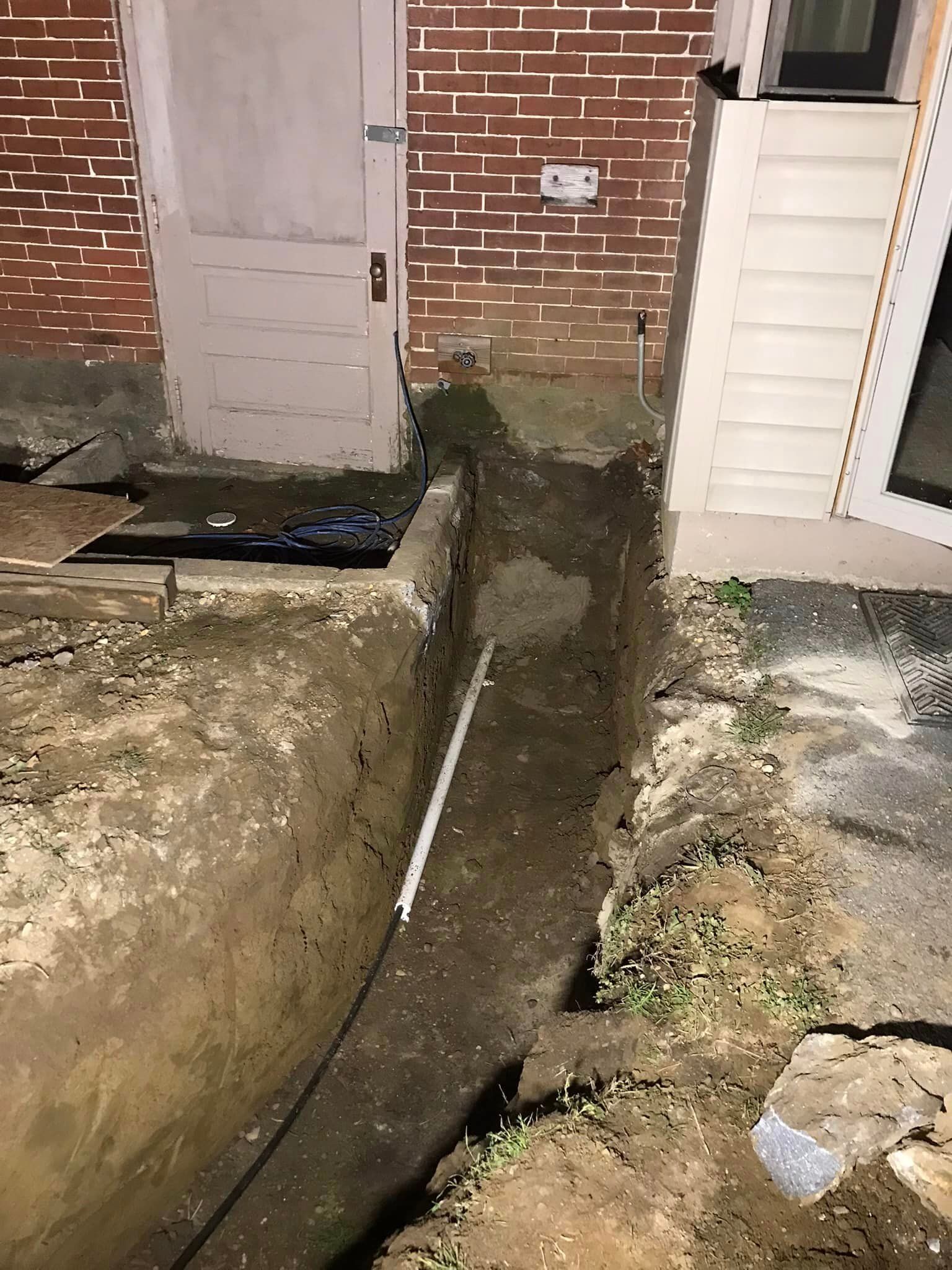 a drain pipe is being installed in the dirt in front of a brick building .