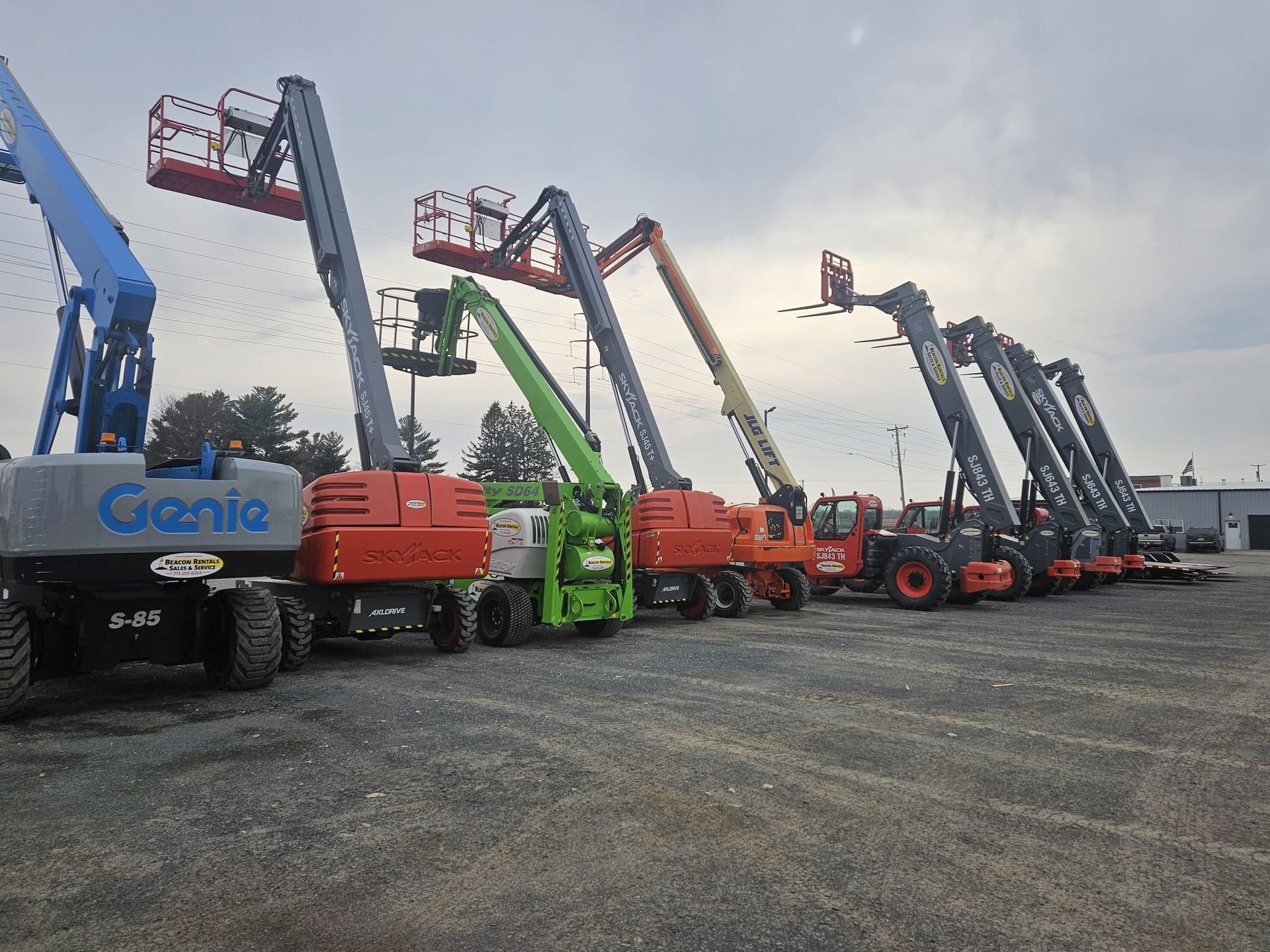 A row of genie lifts are parked in a parking lot.