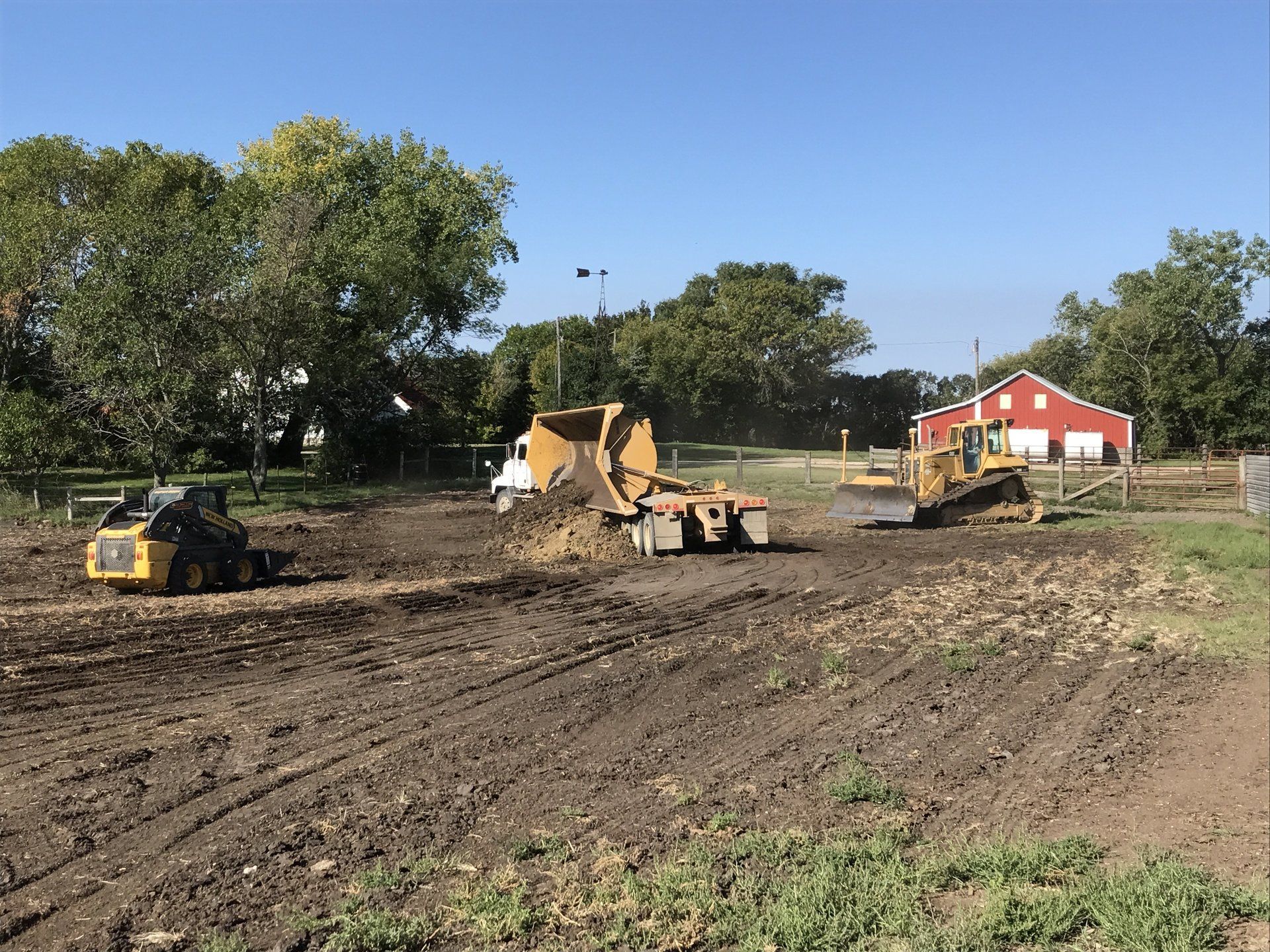 A bulldozer is moving dirt in a field with a red barn in the background.