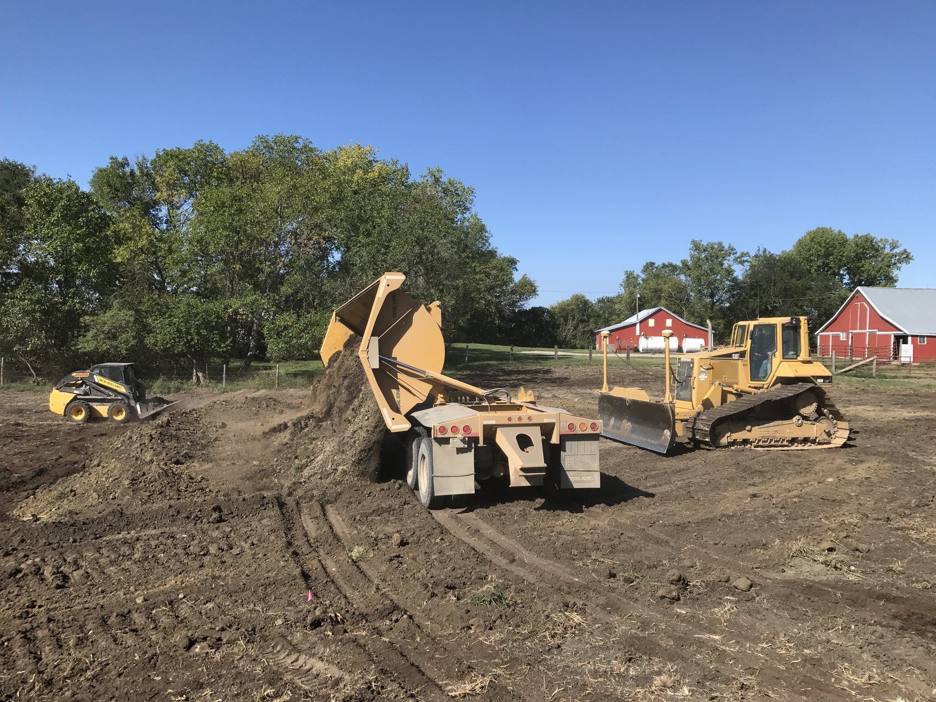 A bulldozer is loading dirt onto a trailer in a dirt field.