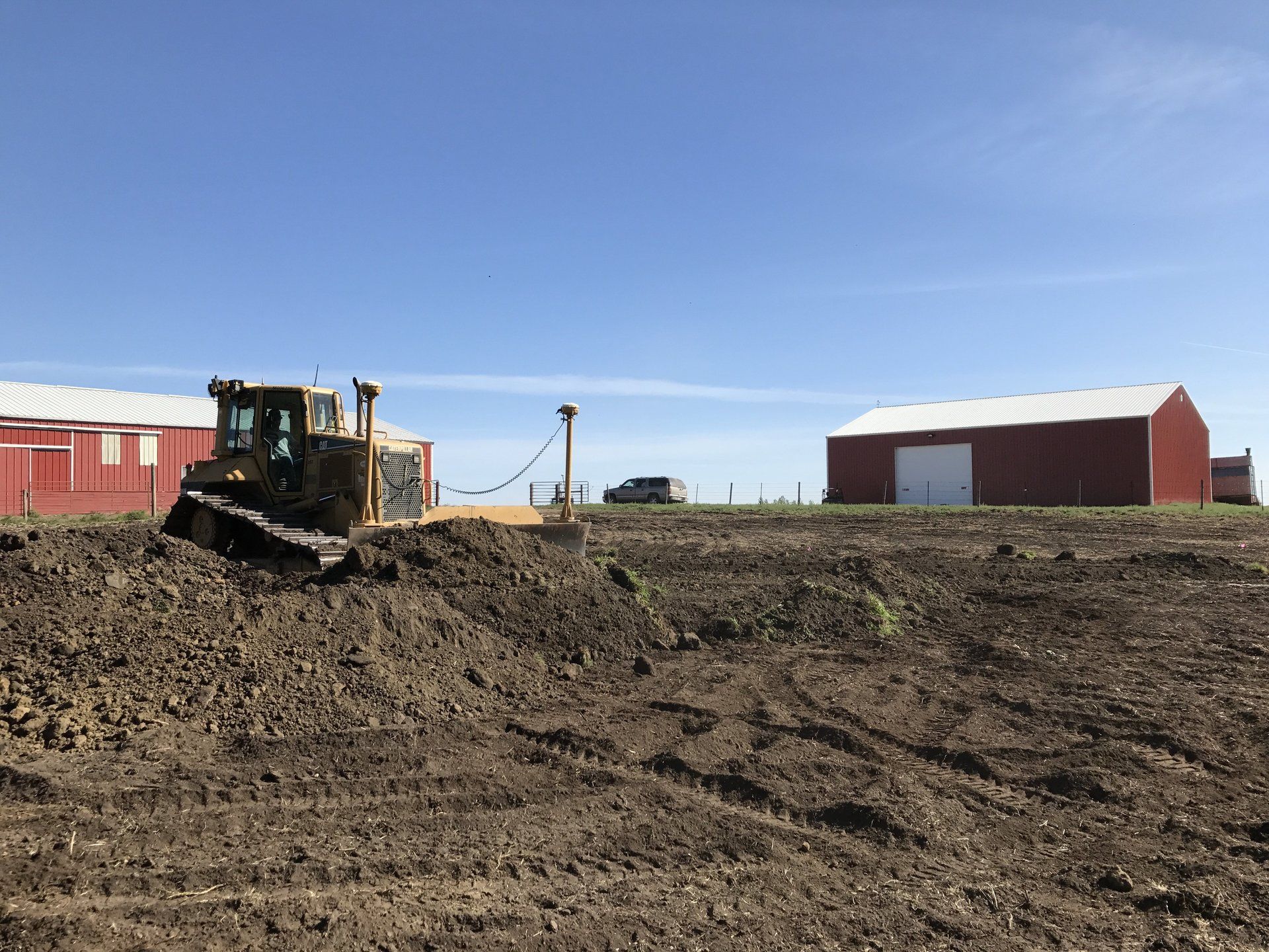 A bulldozer is moving dirt in a field next to a red barn.