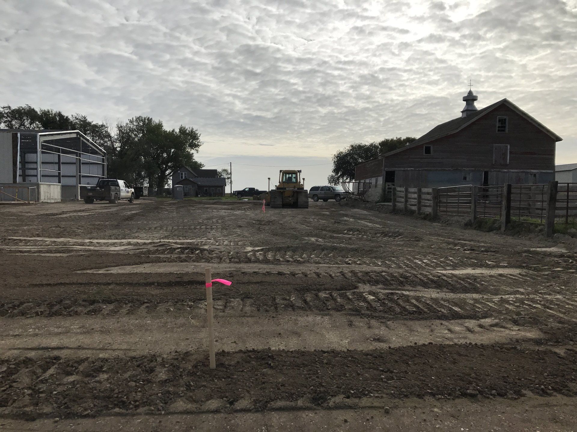 A tractor is driving down a dirt road in front of a barn.