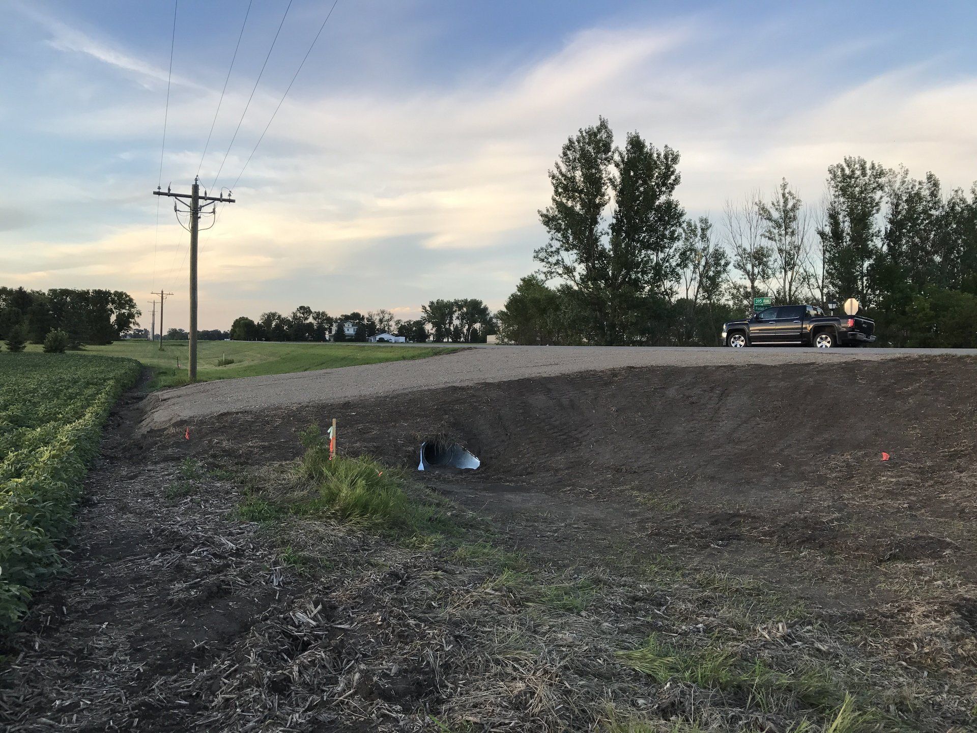A car is driving down a dirt road next to a field