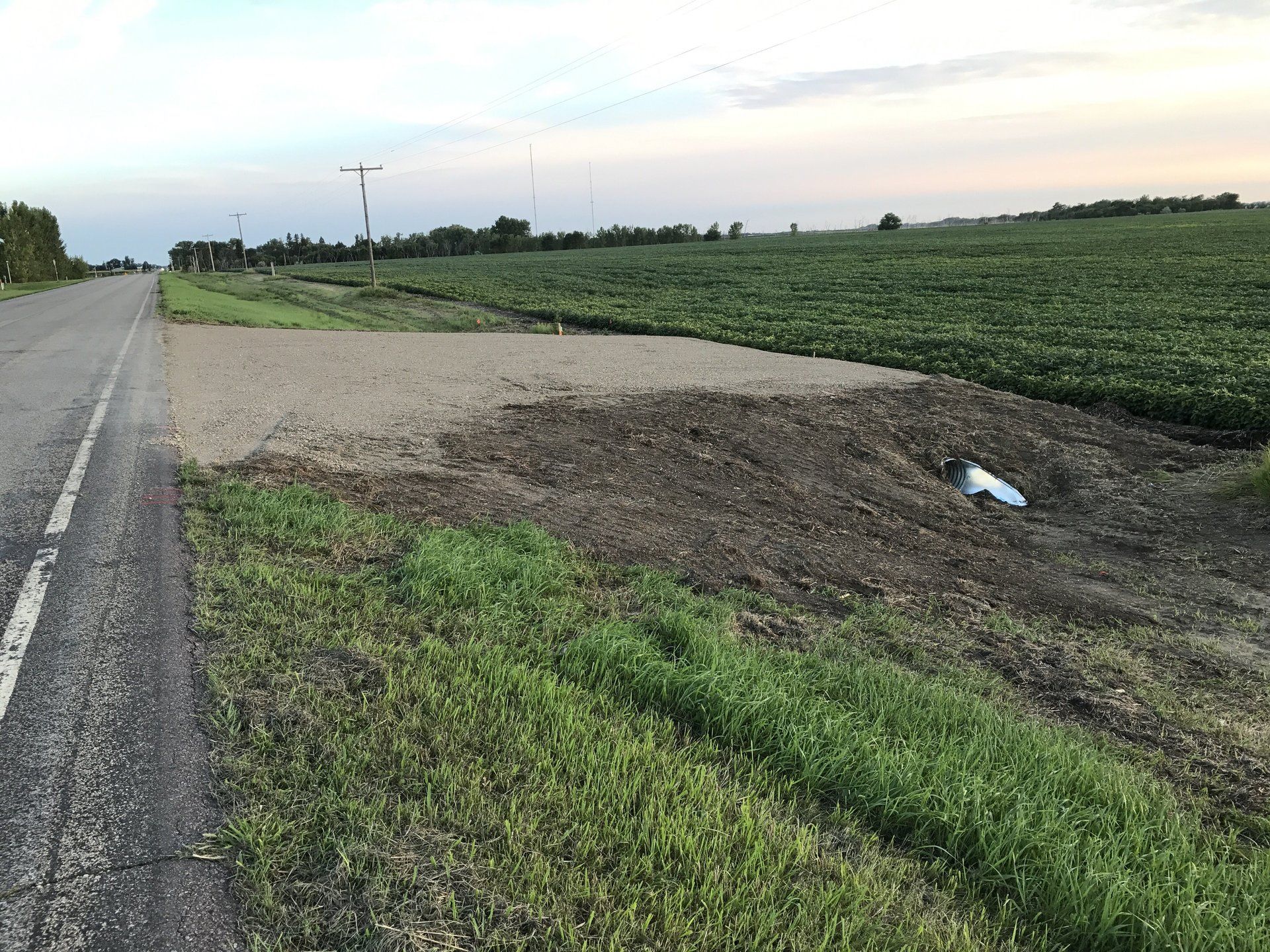 A car is sitting on the side of the road next to a field.