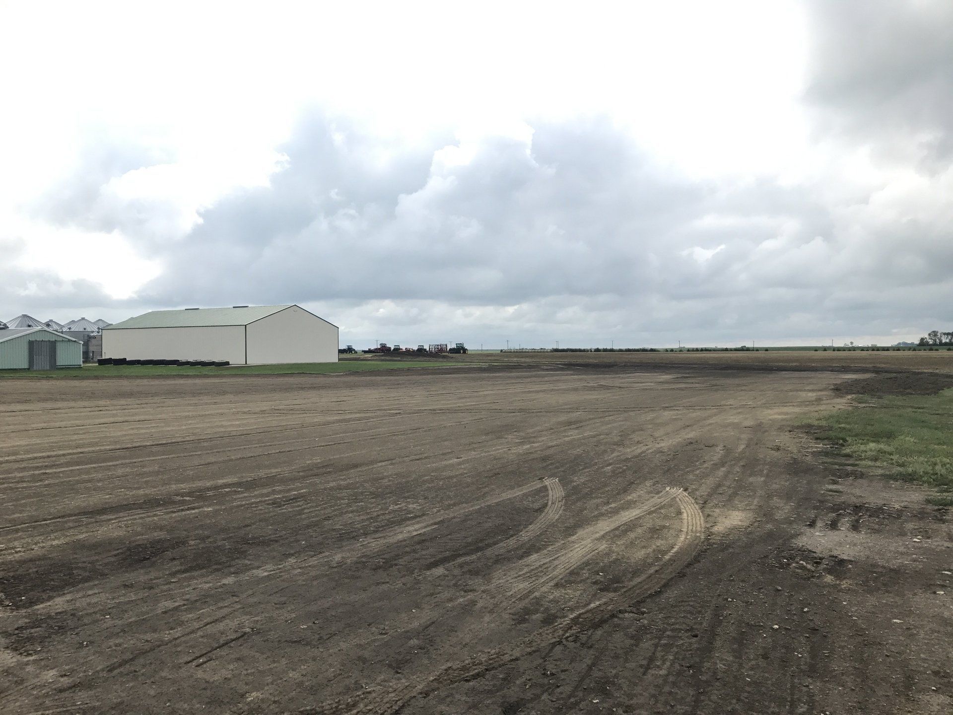 A dirt road going through a field with a building in the background.