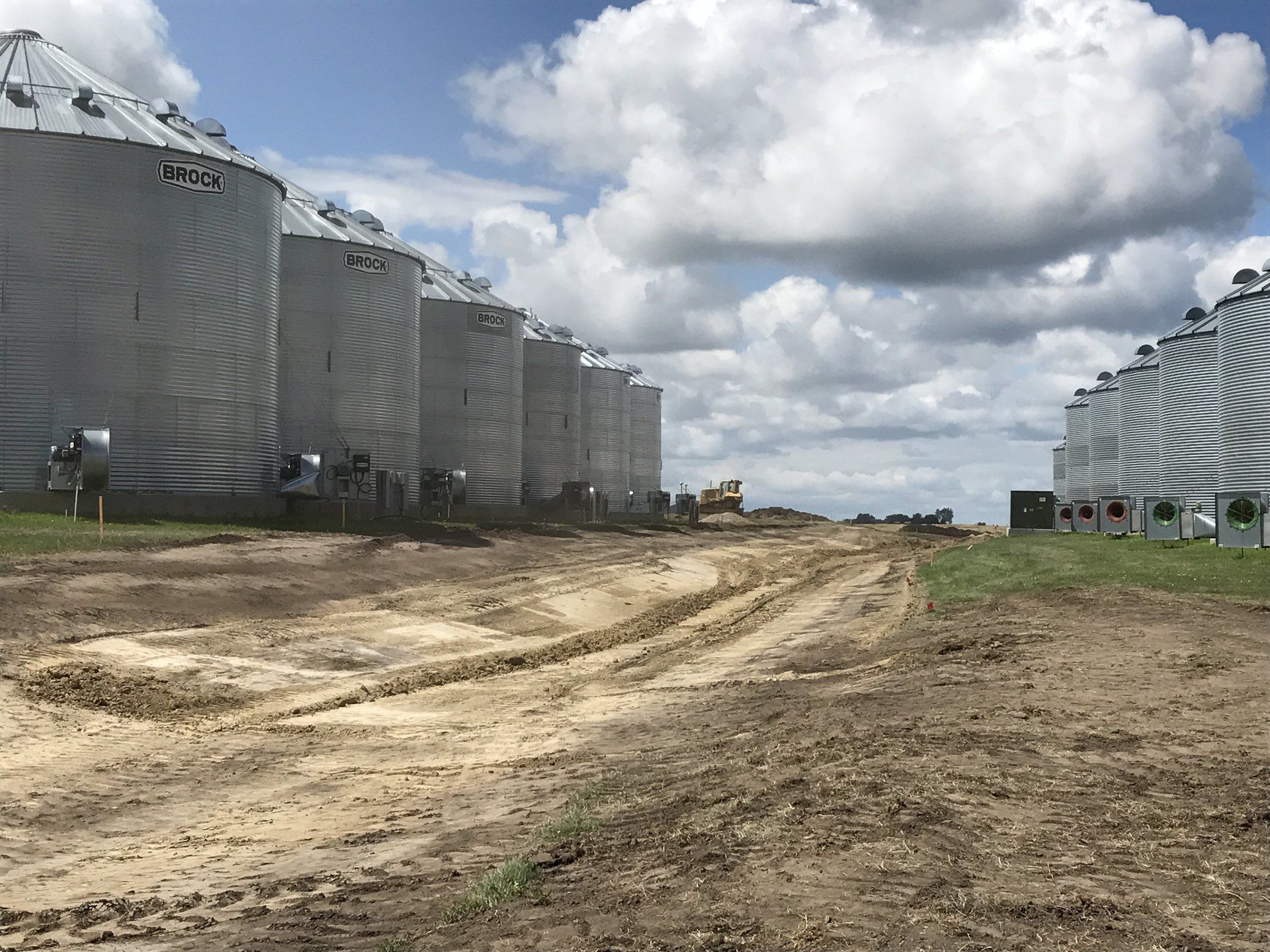 A dirt road leading to a row of silos on a farm.