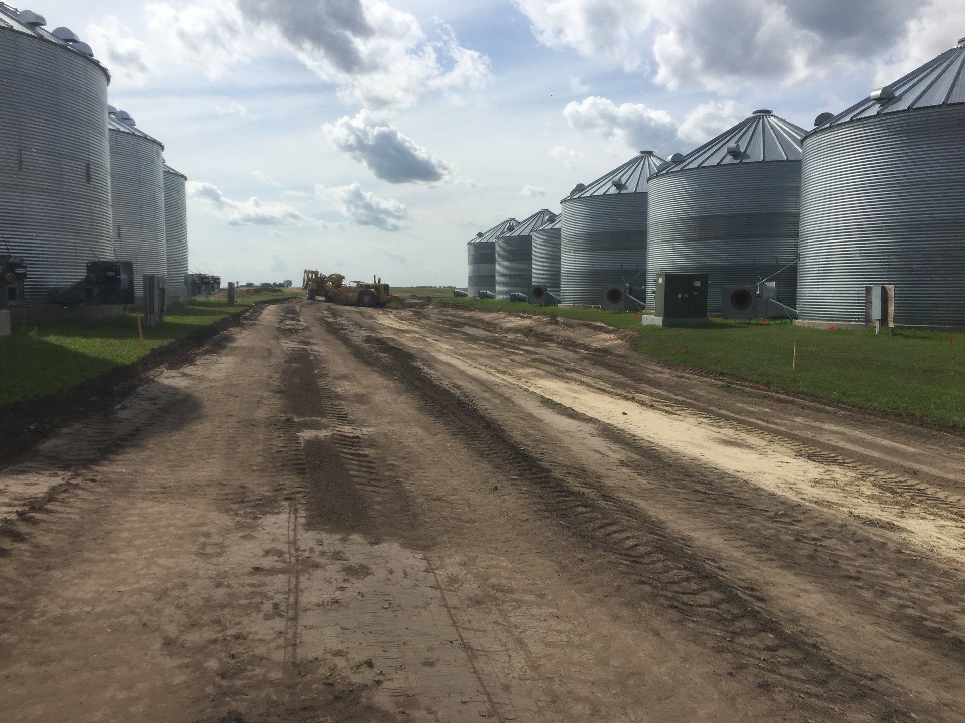 A dirt road leading to a row of silos on a farm.