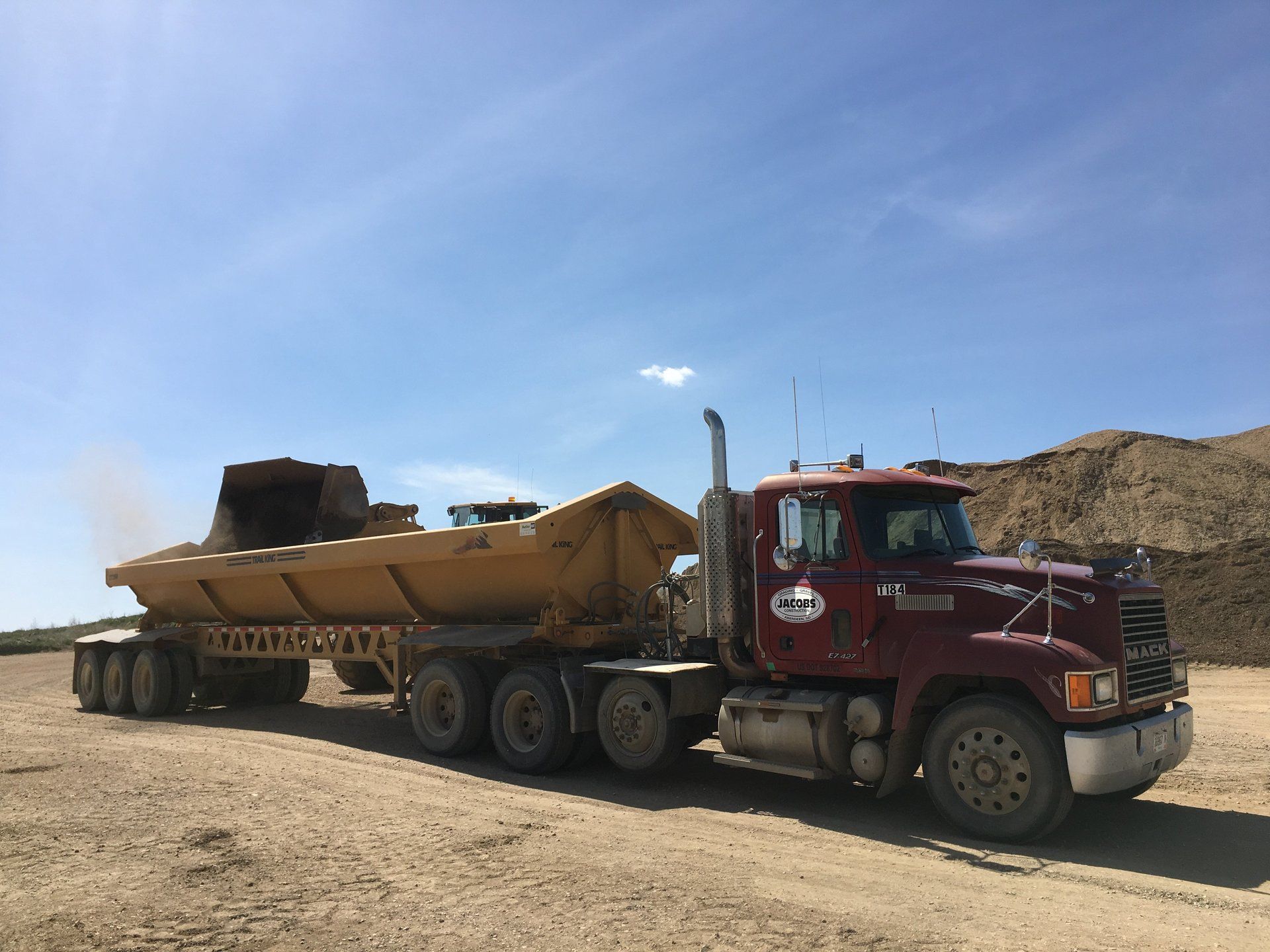 A red dump truck is driving down a dirt road.