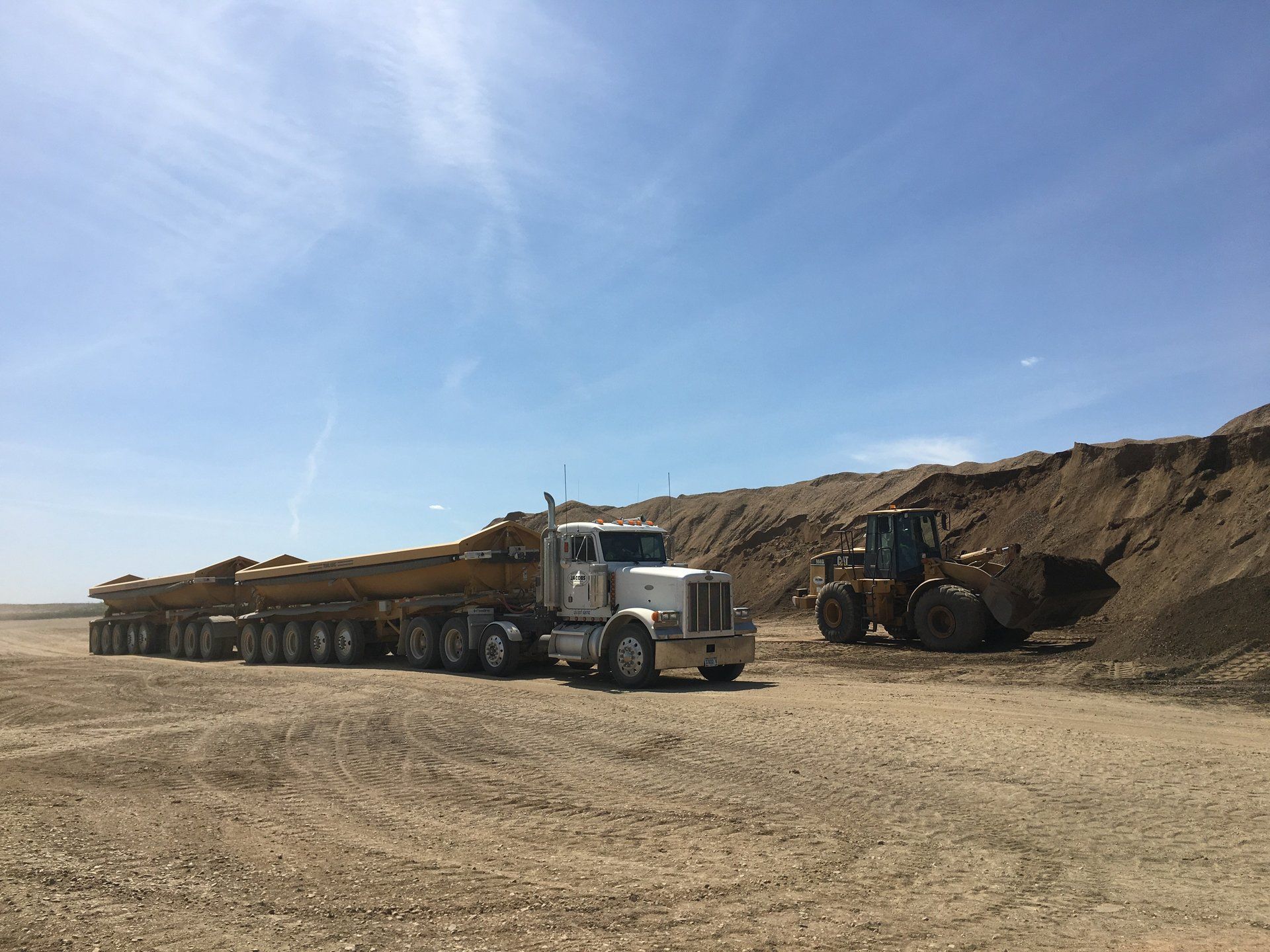 A semi truck is parked in a dirt field next to a bulldozer.