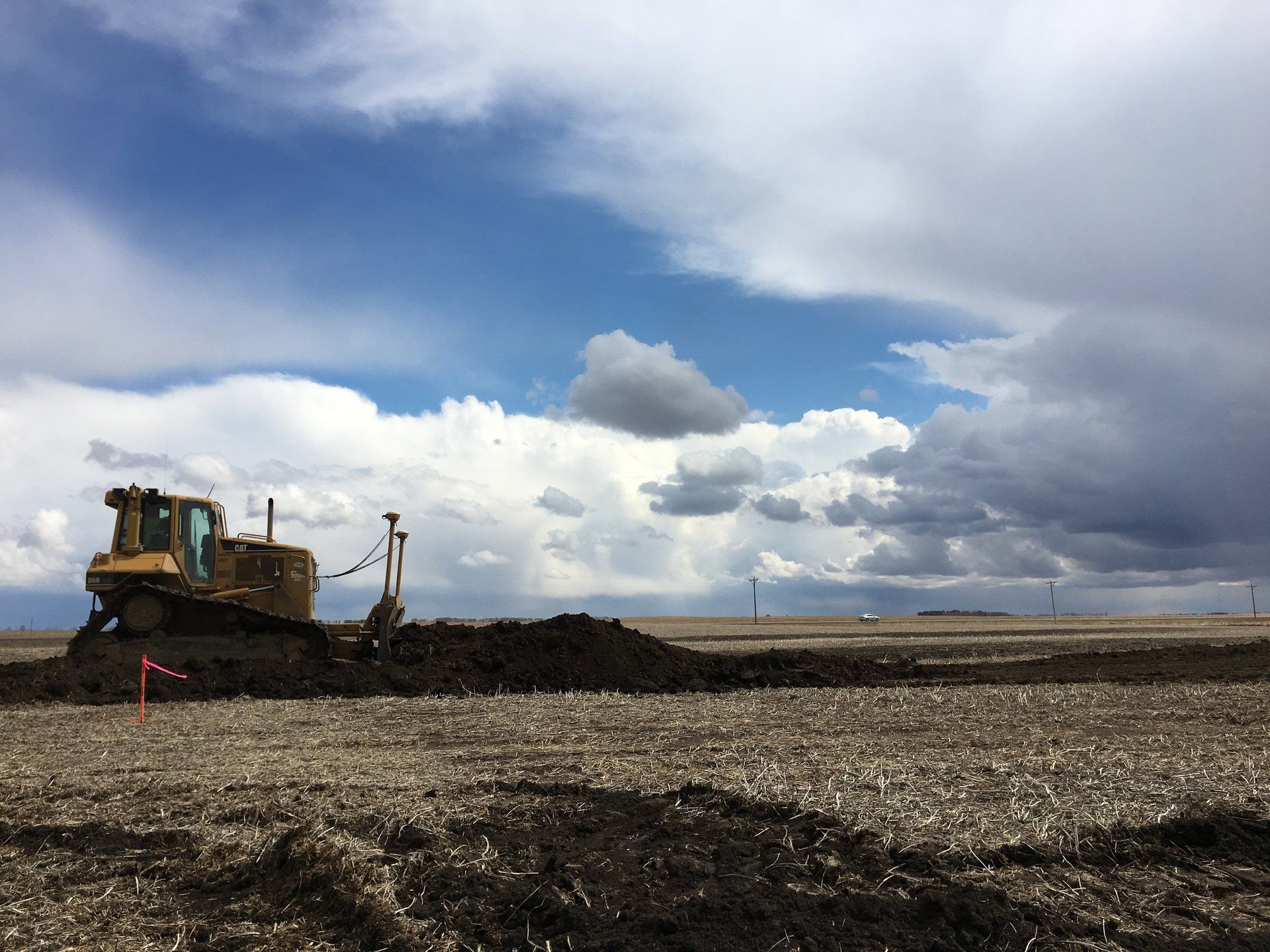 A bulldozer is plowing a field with a cloudy sky in the background
