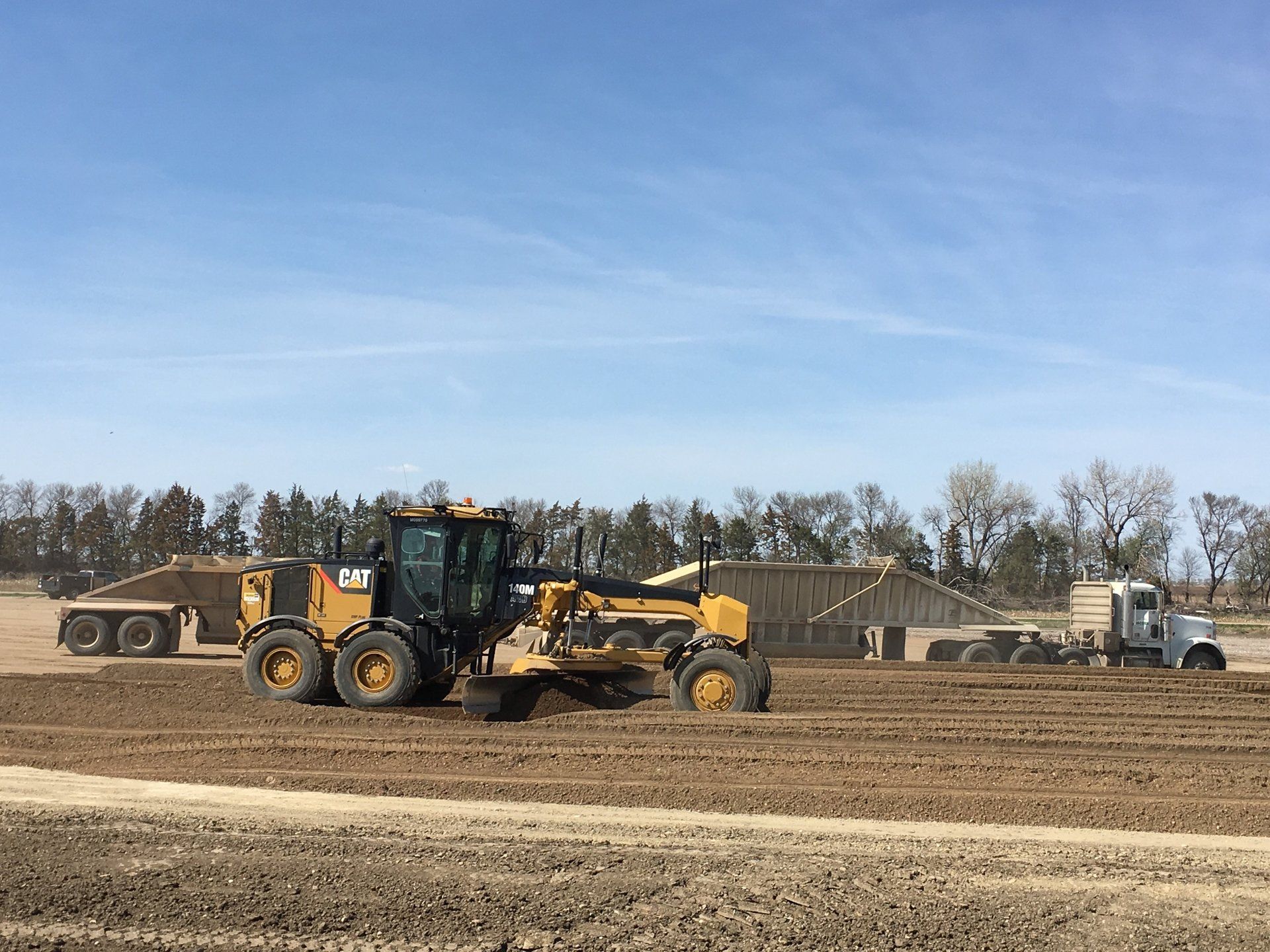 A bulldozer is plowing a dirt field next to a truck.