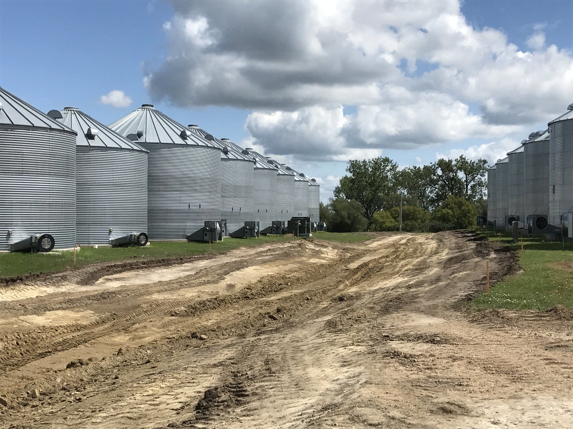 A dirt road leading to a row of silos on a farm.