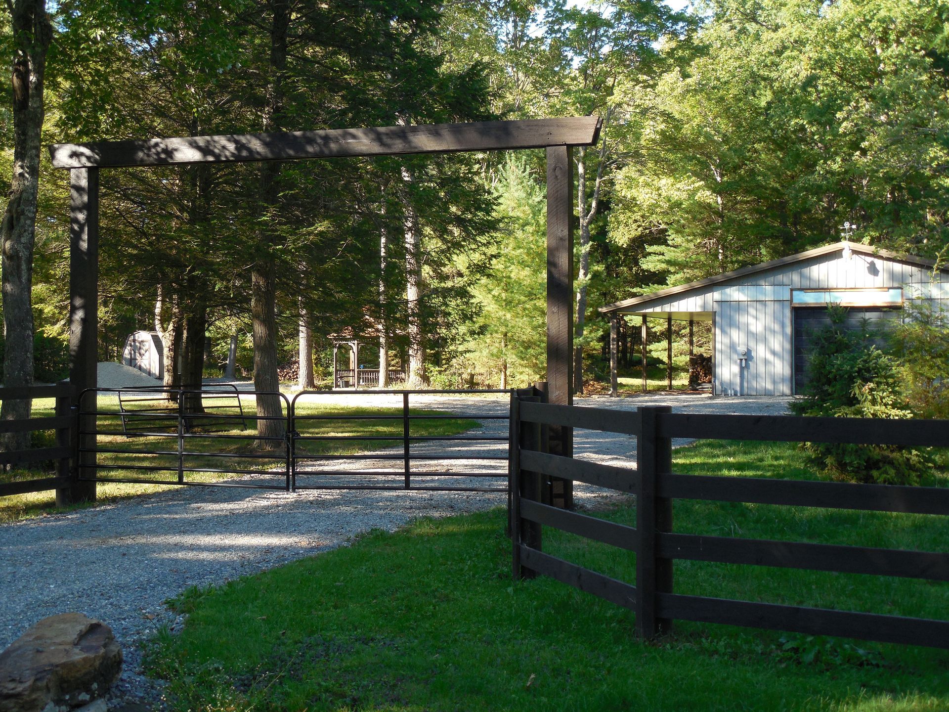 A black fence surrounds a driveway leading to a house