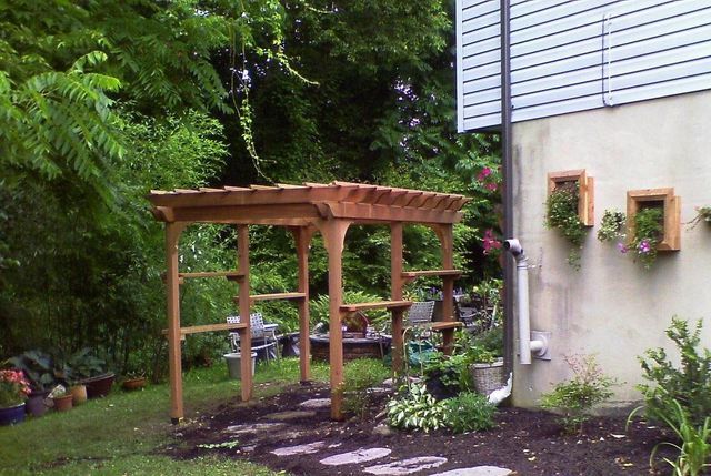 A wooden pergola is in the backyard of a house