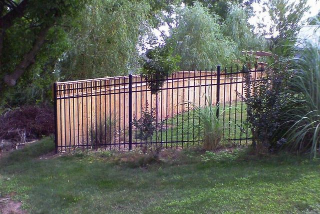 A metal fence with a wooden fence behind it