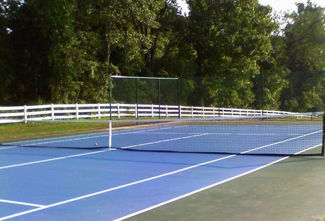 A blue tennis court with a white fence in the background