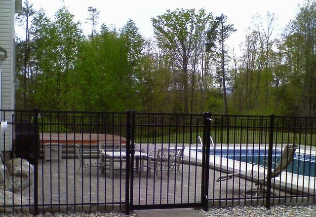 A black fence surrounds a patio with a pool in the background