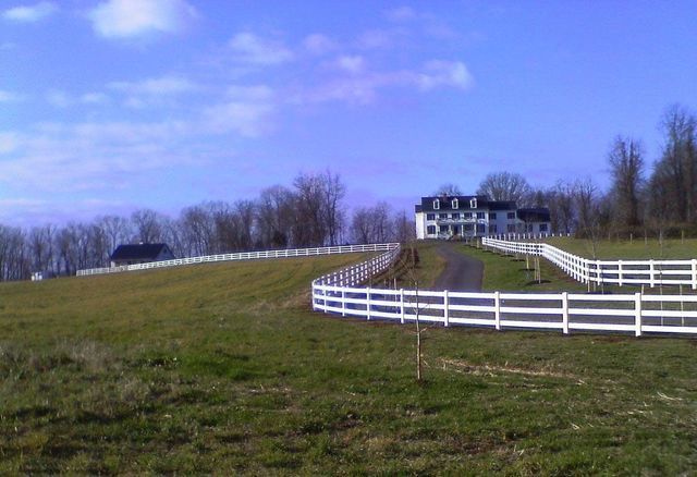 A white fence surrounds a grassy field with a house in the background.