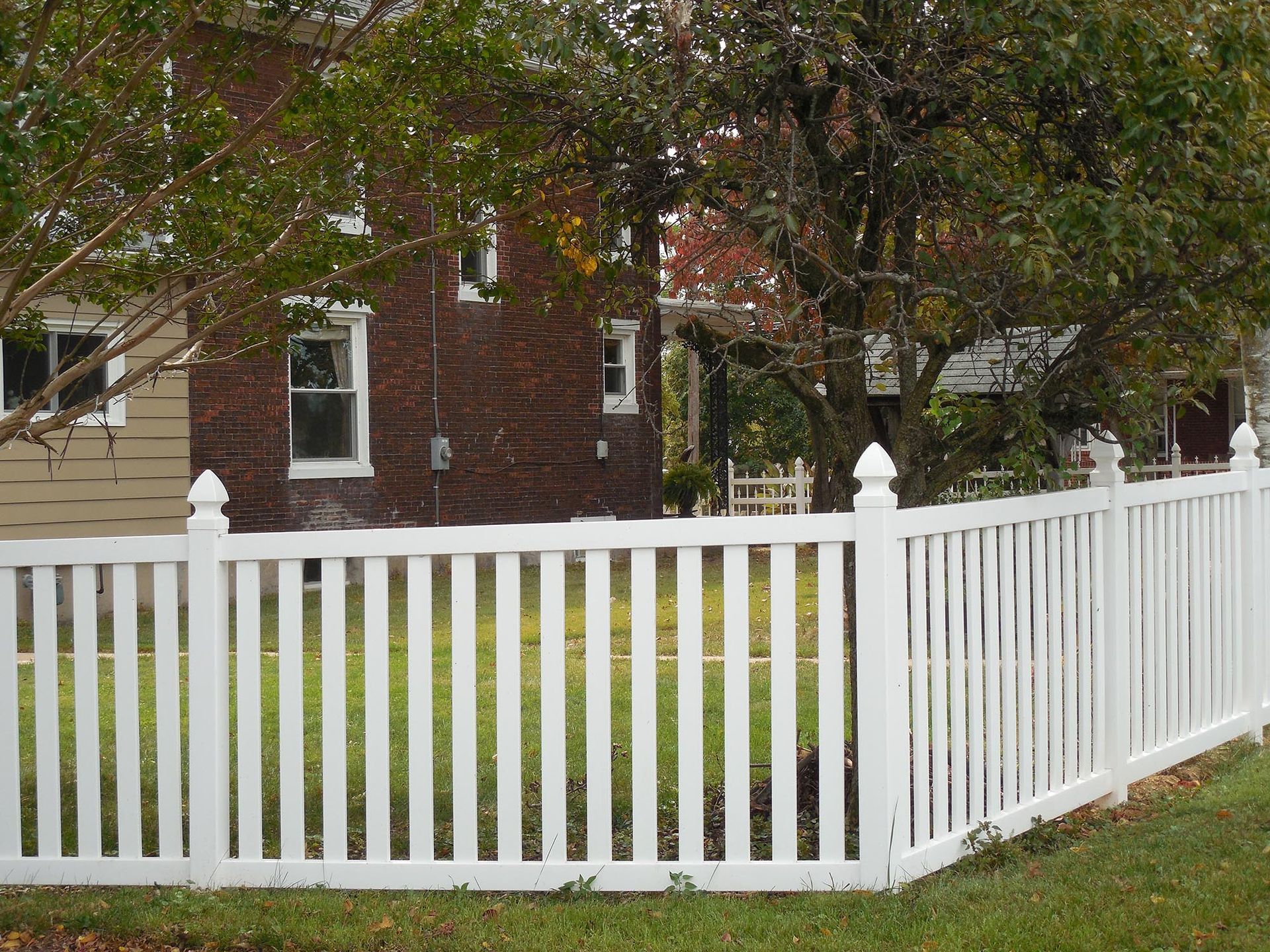 A white picket fence is in front of a brick house.
