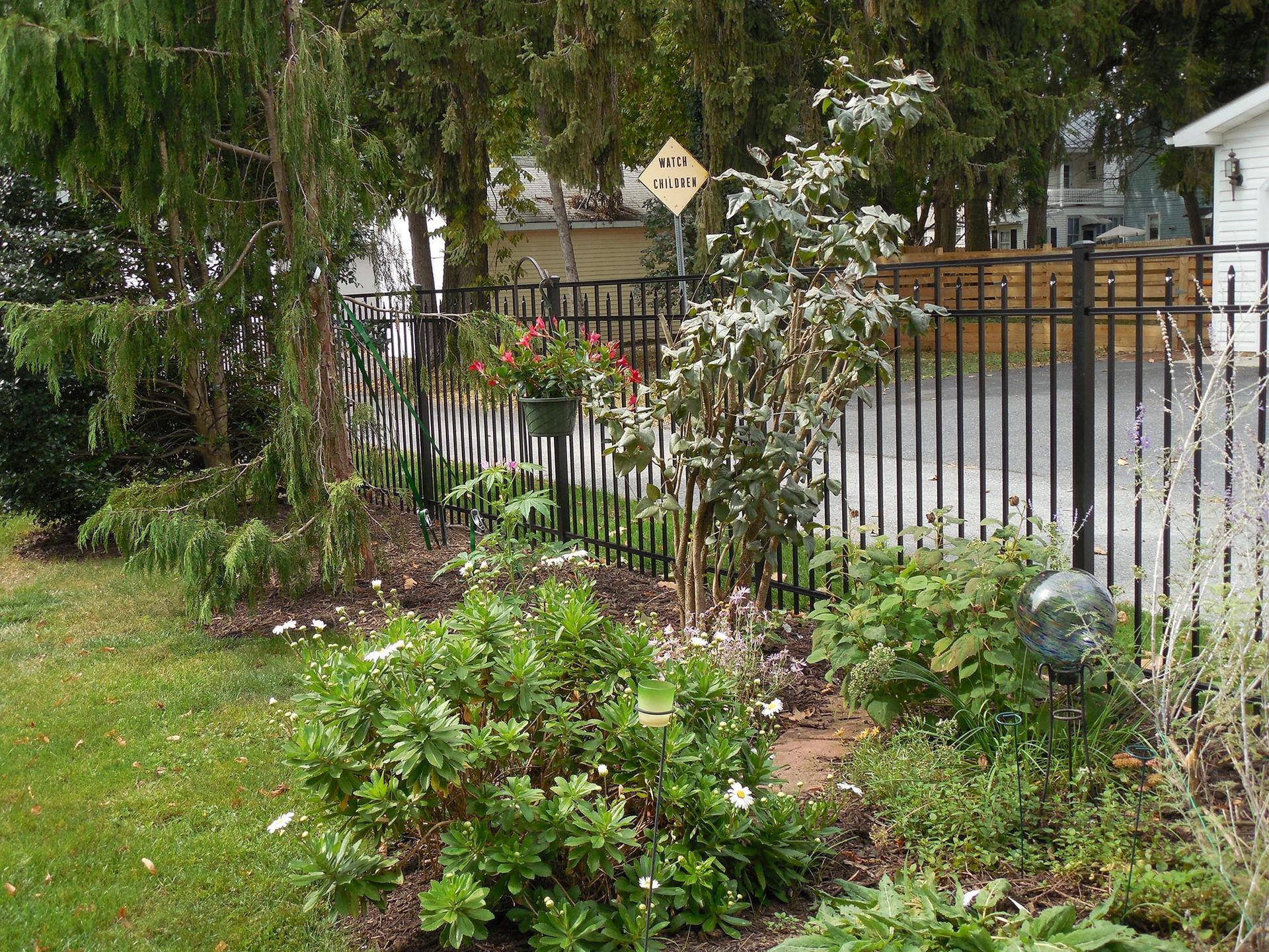 A fence surrounds a garden with lots of plants and trees.