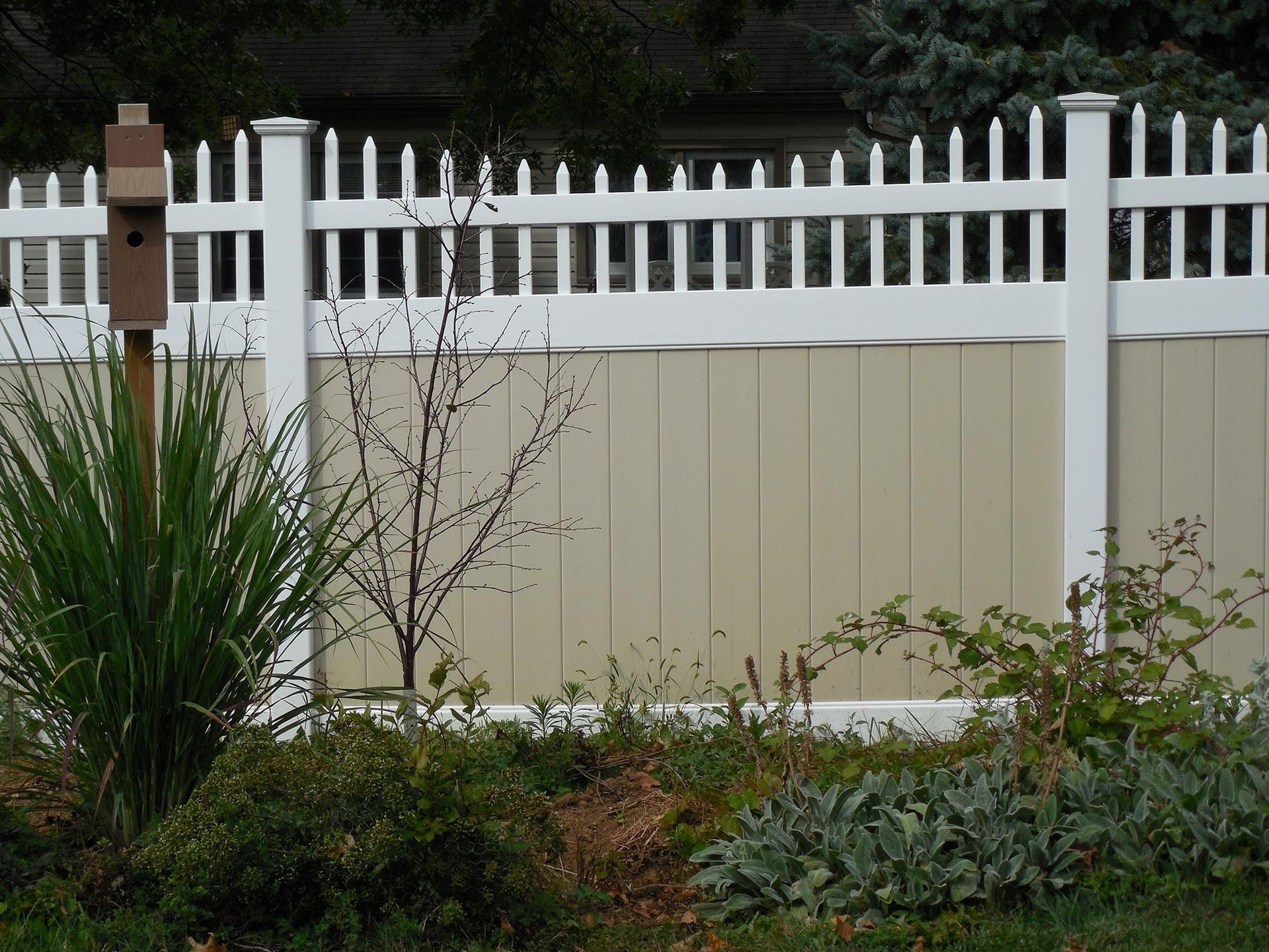 A white and tan fence with a birdhouse in the background