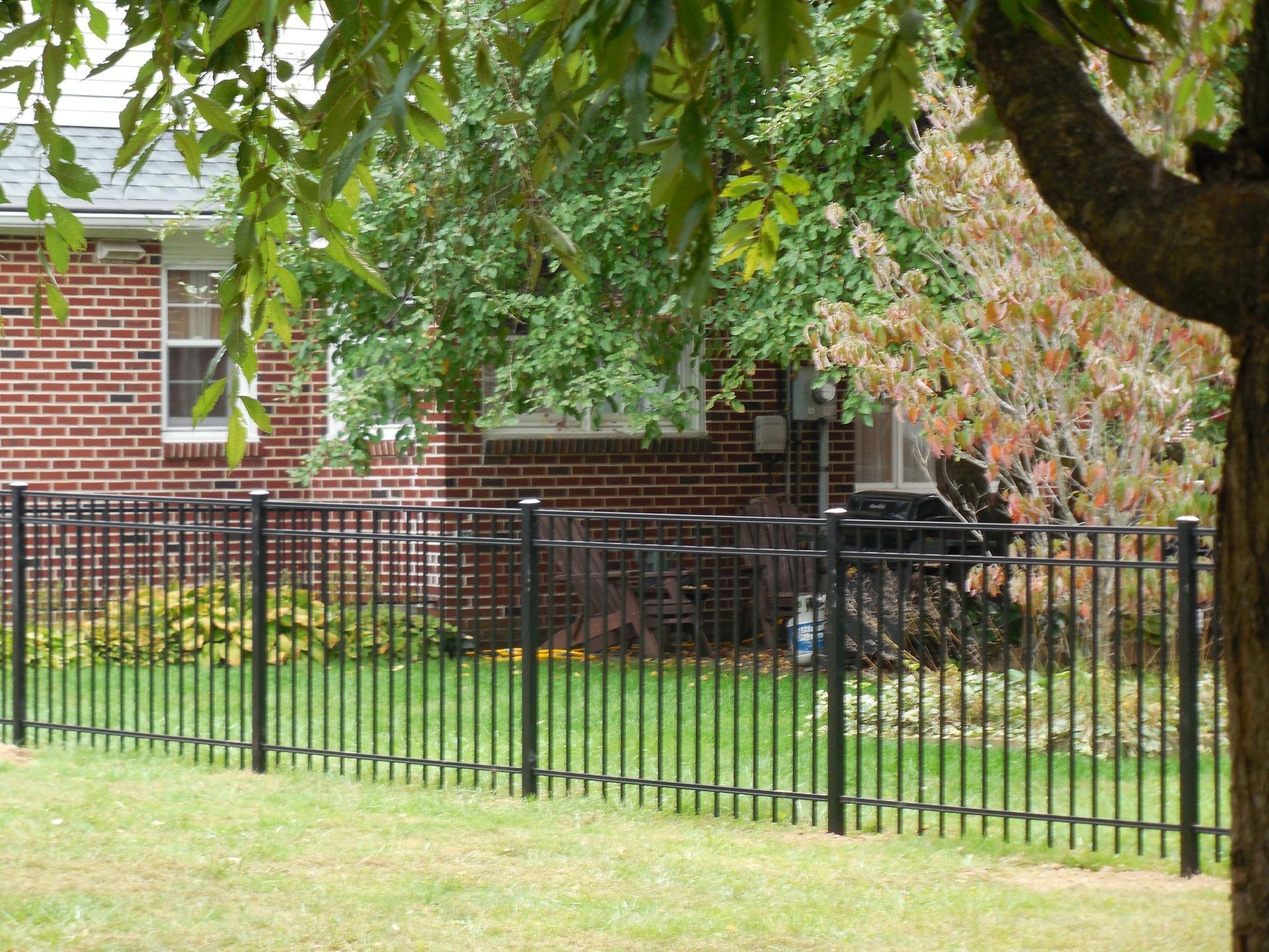 A black fence surrounds a lush green yard in front of a brick house.